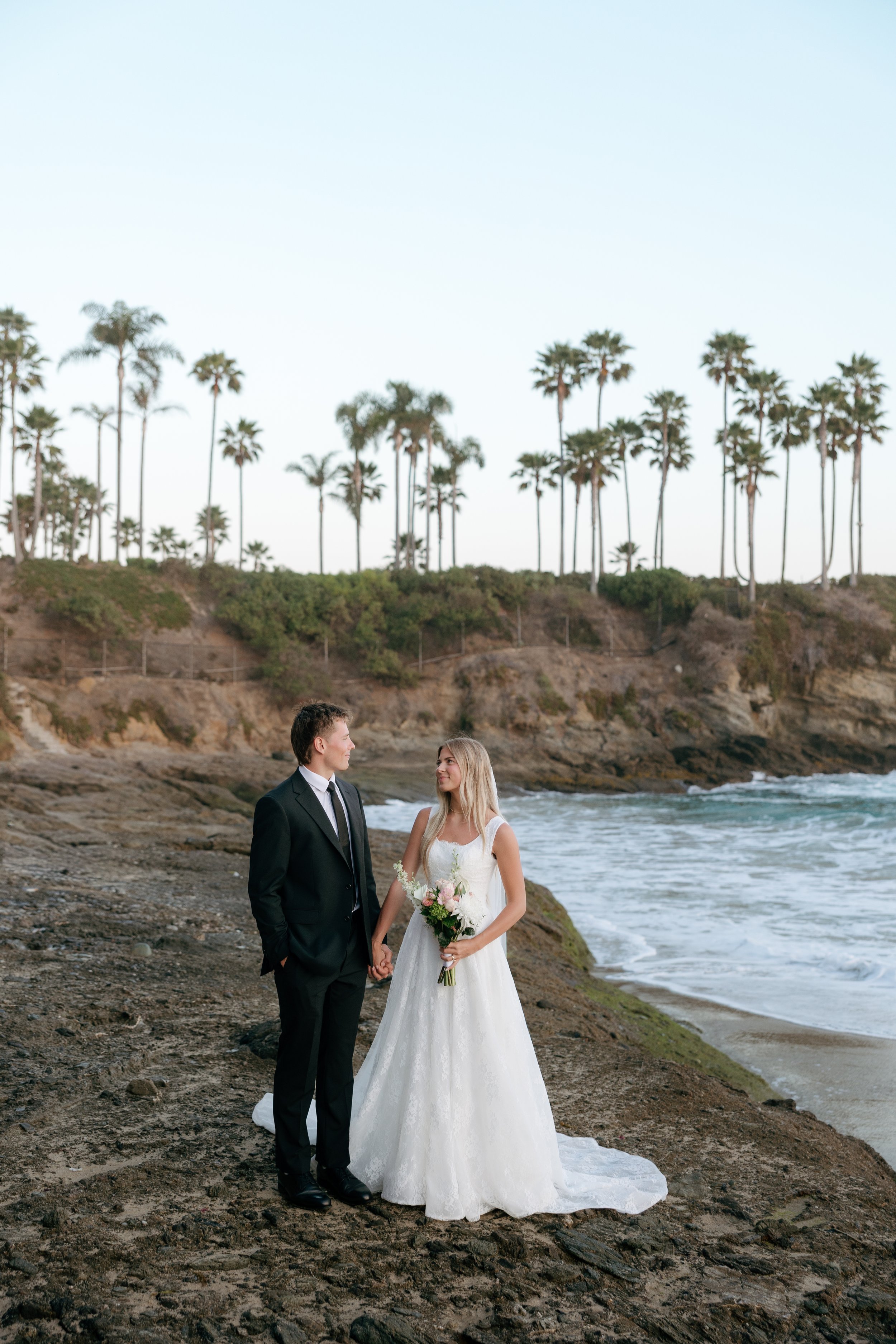 couple posing on cliffs in bridal attire in southern california surrounded by palm trees