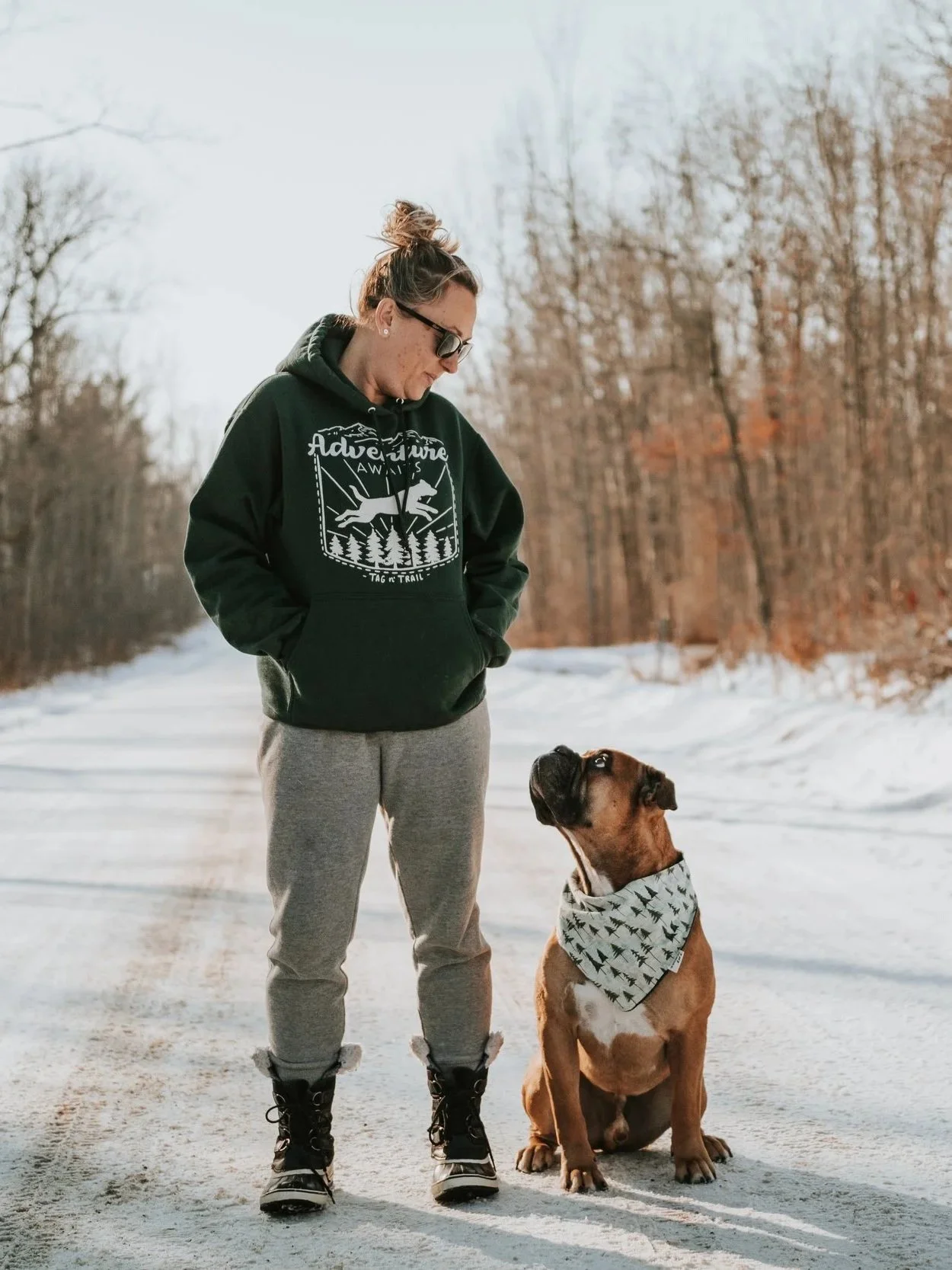 Woman standing on a road looking down at her fawn and black Olde English Bulldogge sitting beside her.