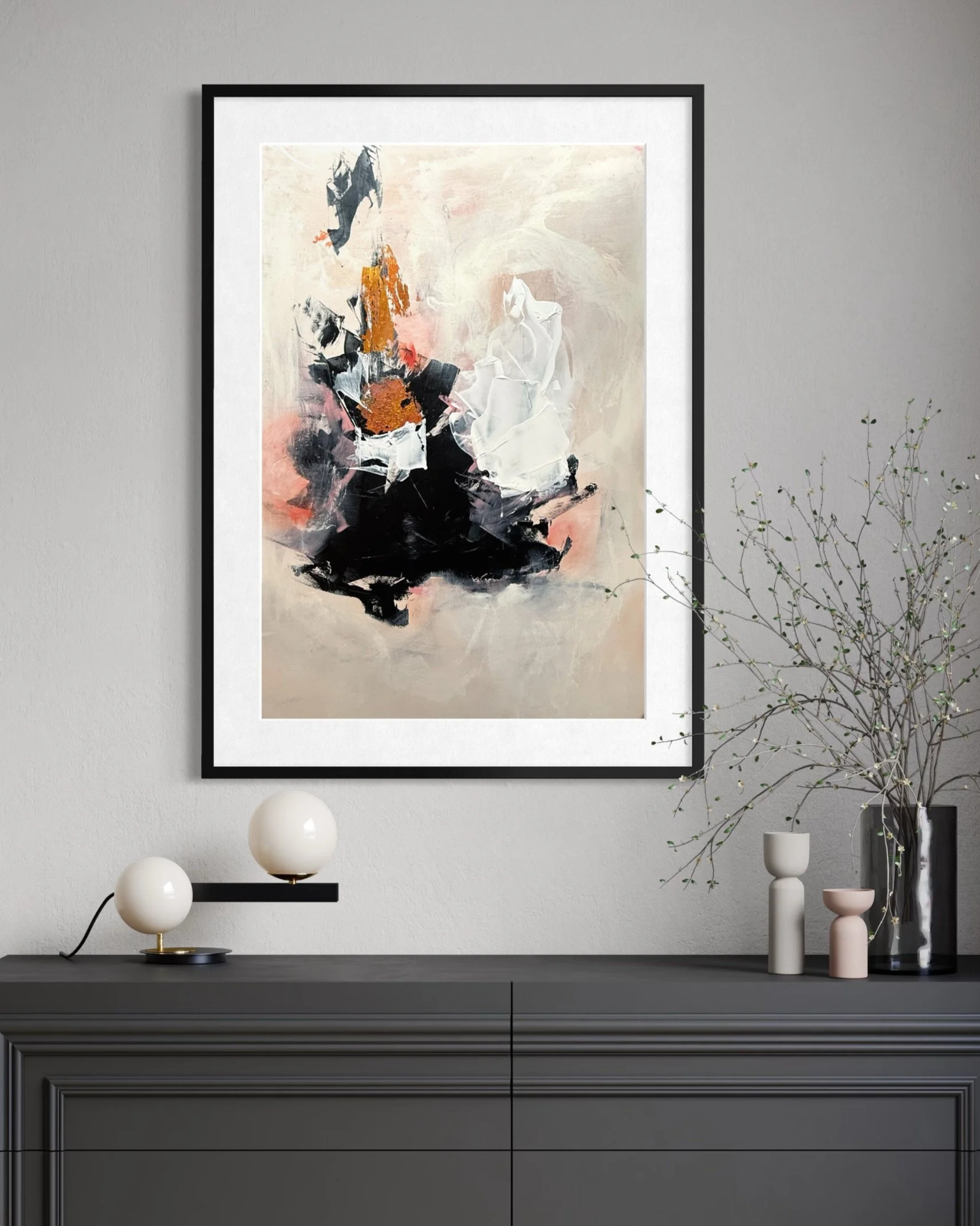 Abstract painting with beige, black, white, and orange colors hanging on a gray wall above a gray cabinet, with decorative vases and a branch in a tall vase.