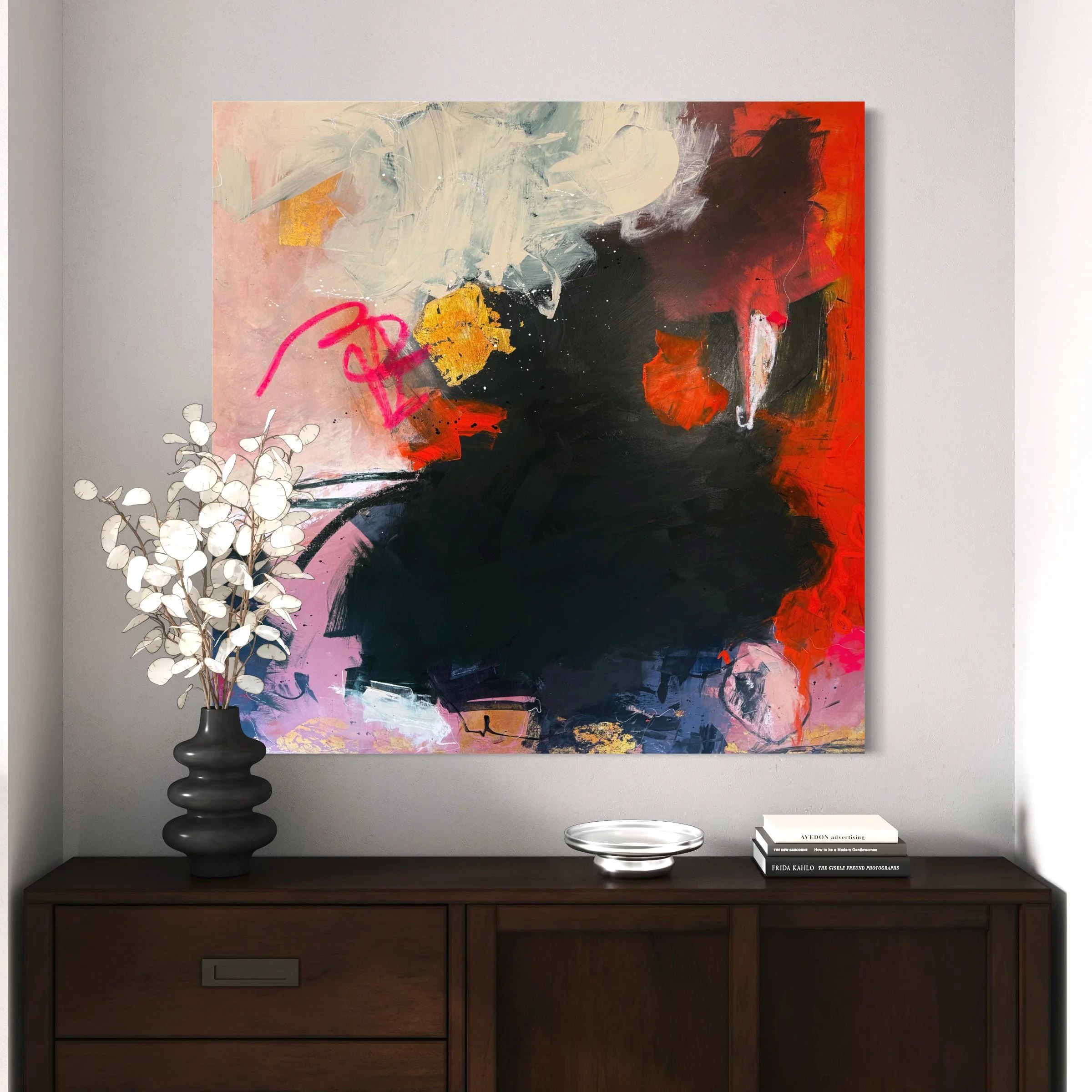 Abstract colorful painting of a black dog with red, orange, gray, pink, and white accents, hanging on a wall above a wooden sideboard with a decorative black vase with white branches, a silver bowl, and stacked books.