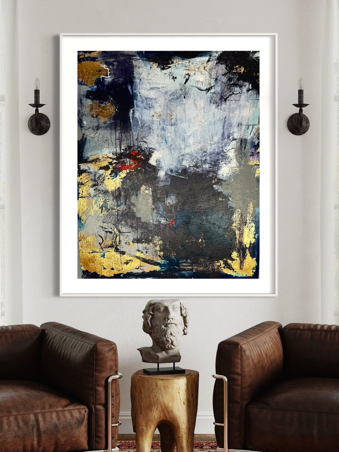 A large abstract painting with dark blue, black, gray, white, and gold colors hangs on a white wall between two black wall sconces in a room with brown leather armchairs. A white bust sculpture sits on a wooden side table below the painting.