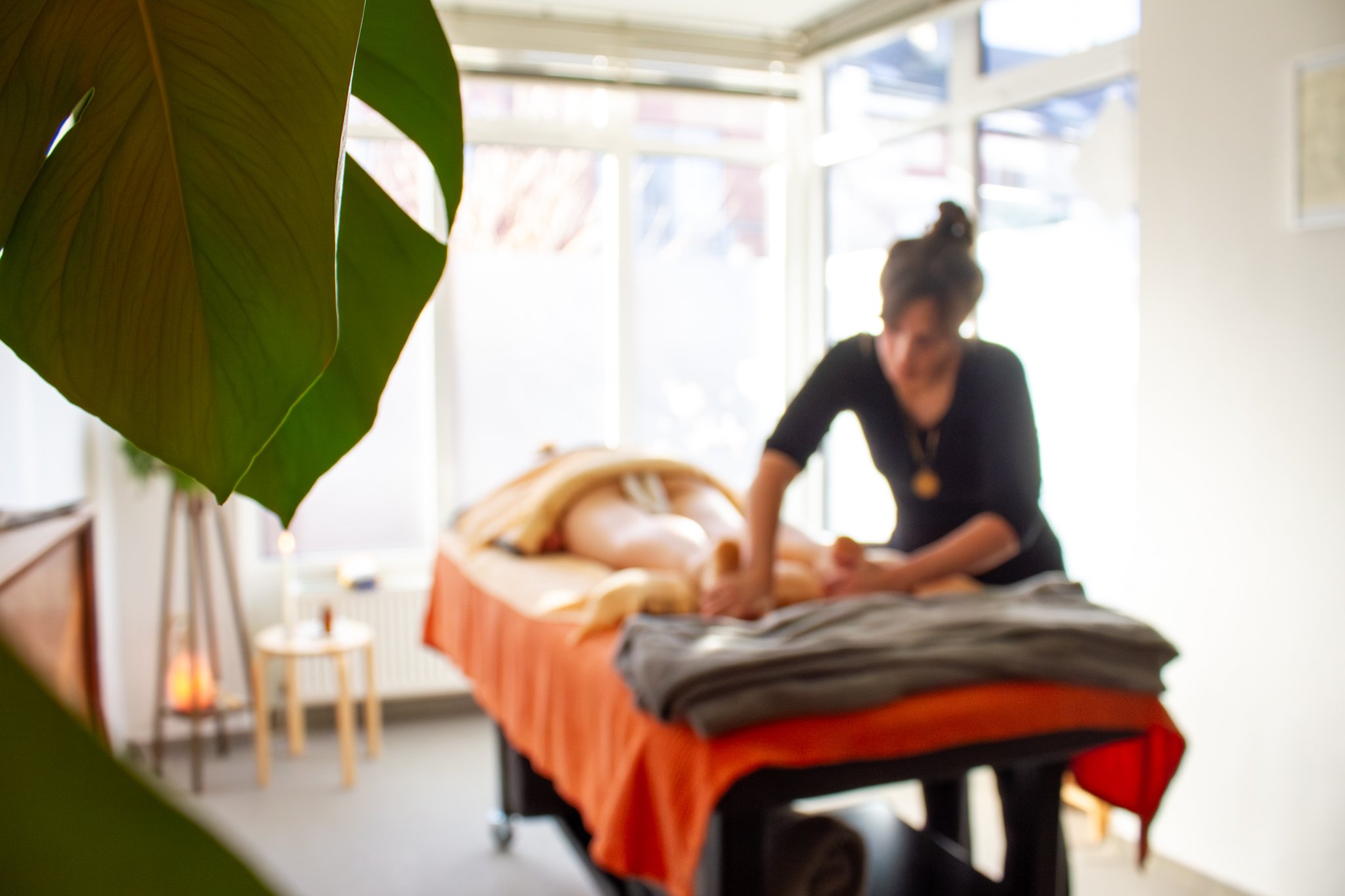 Meta van Ghold geeft een massage aan een persoon die op een tafel ligt in een kamer met grote ramen en planten.