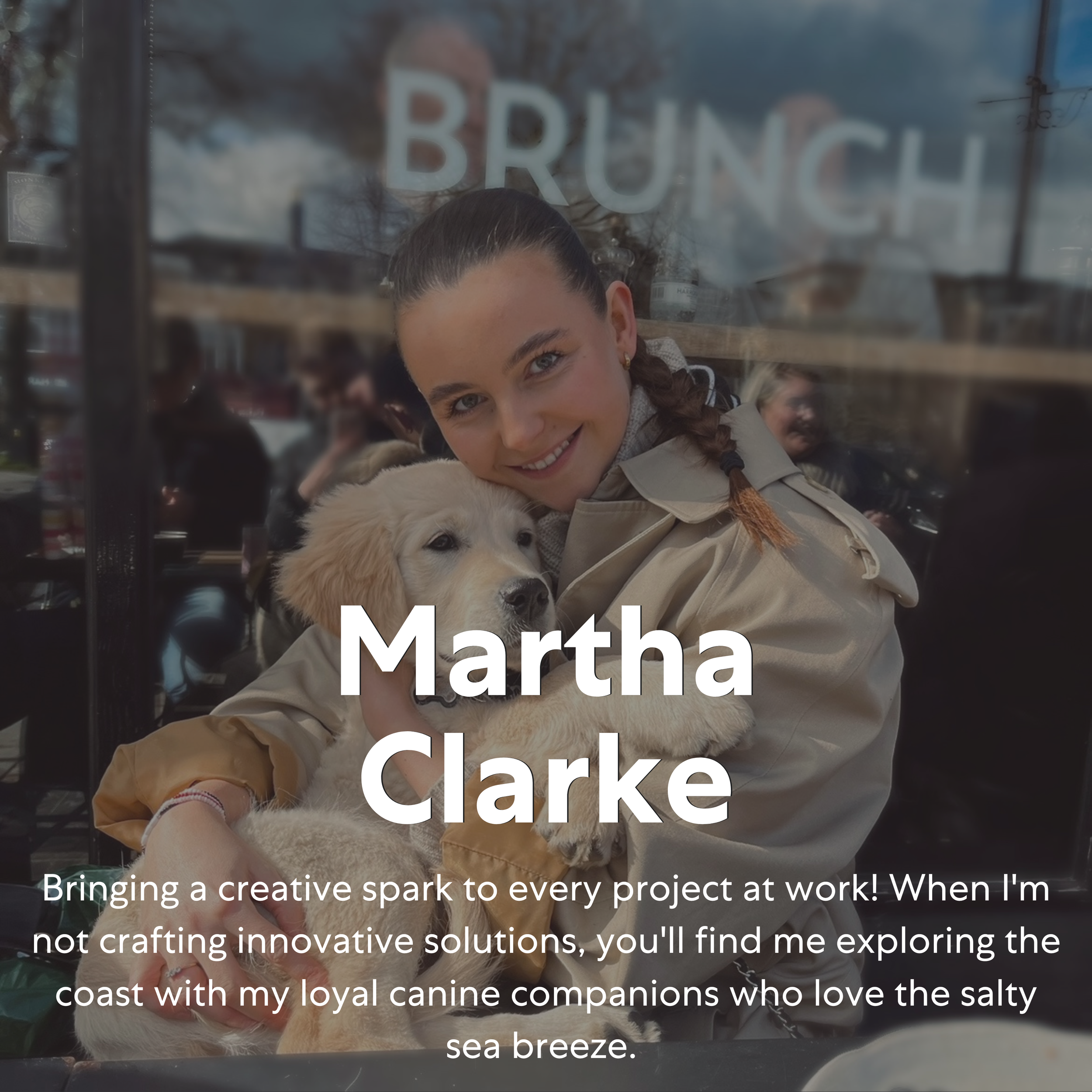A woman with dark hair tied back, smiling and hugging a golden retriever puppy outside of a cafe with a glass window that has the word 'BRUNCH' written on it. The woman is wearing a beige trench coat.