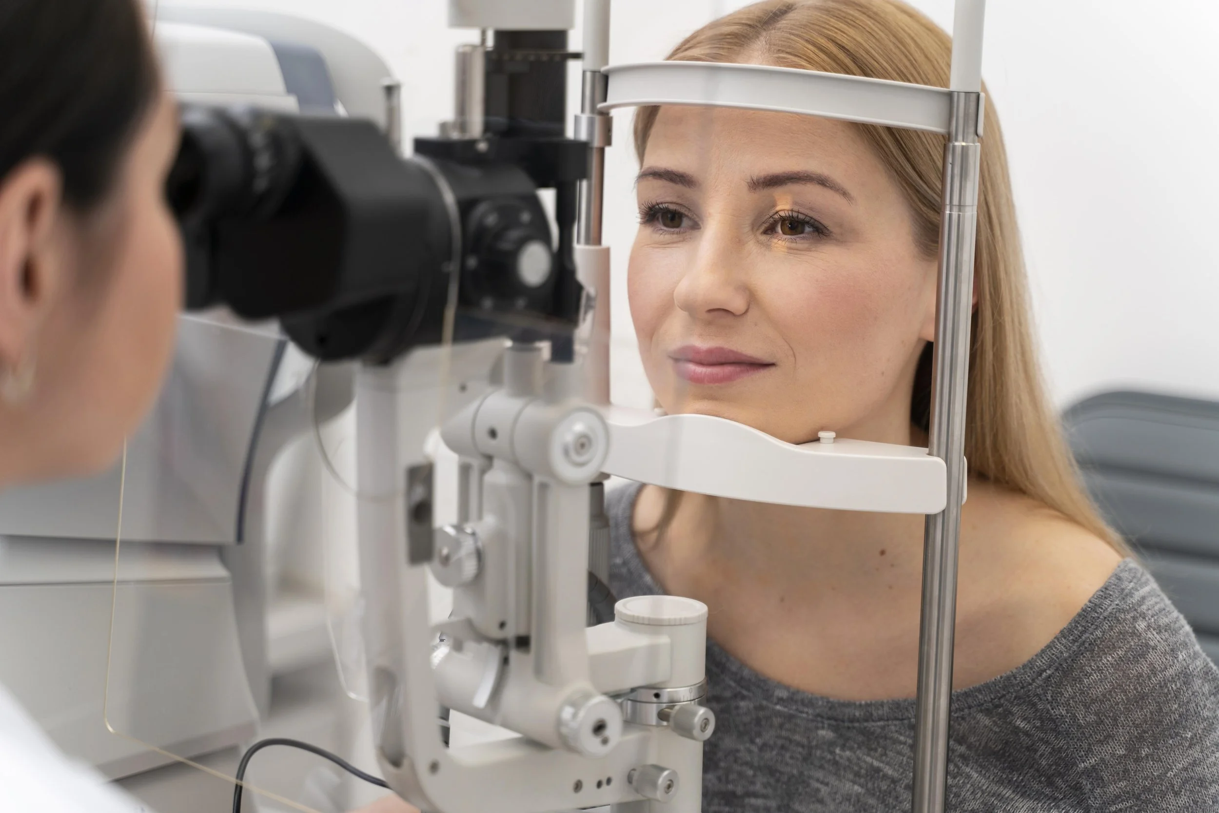 A woman undergoing an eye exam using a slit lamp at an optometrist's office.