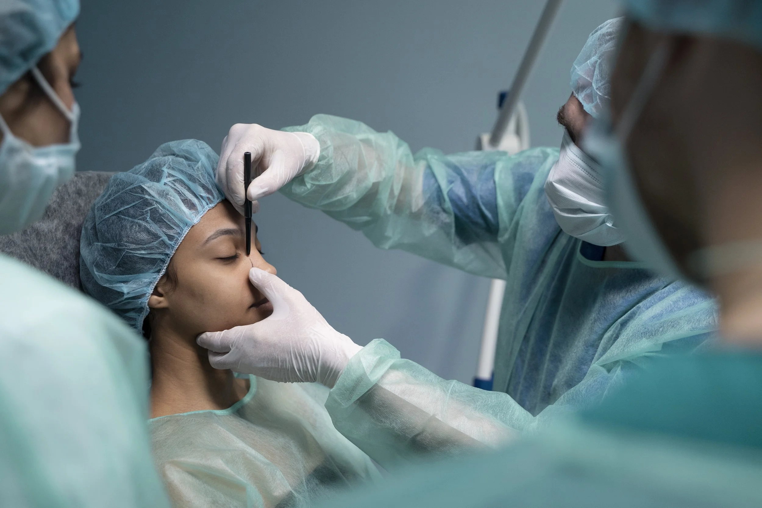 Medical team performing a procedure on a woman with her eyes closed, in a clinical setting.