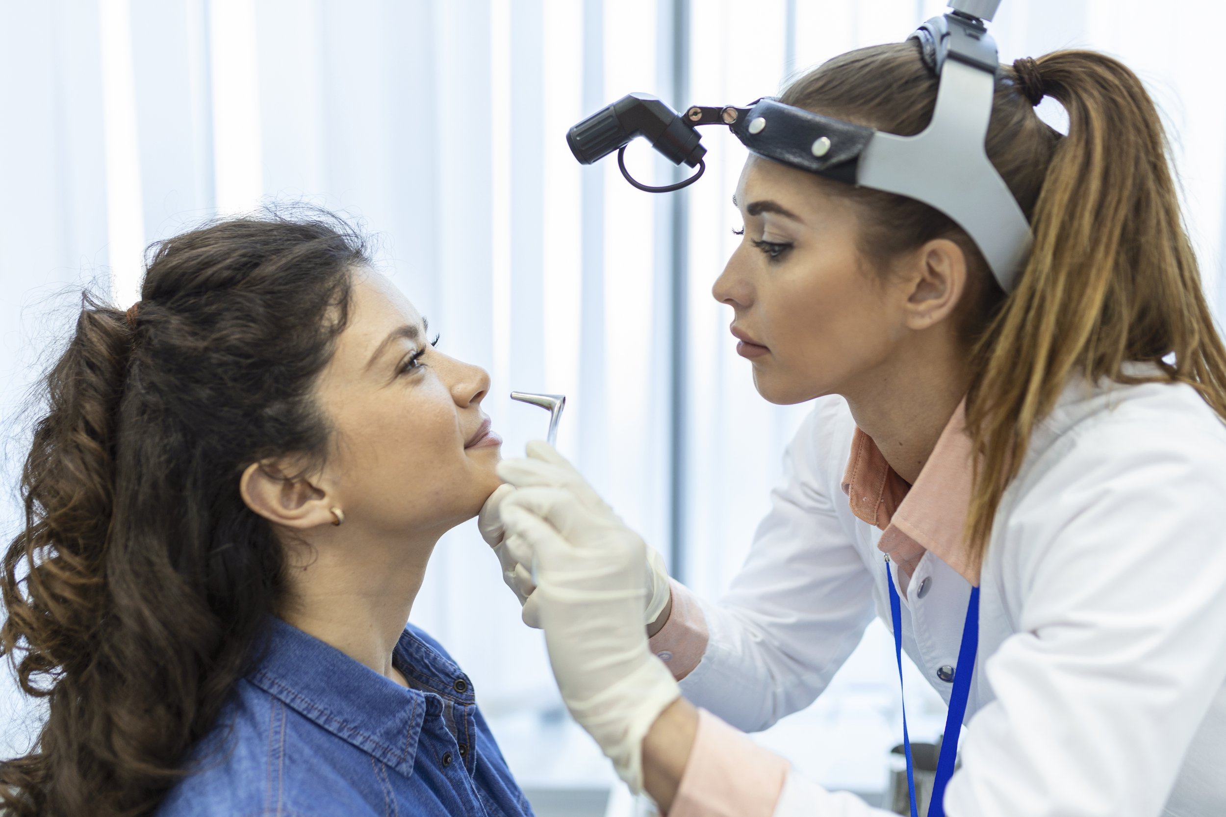 Dentist examining a woman's teeth in a clinical setting.