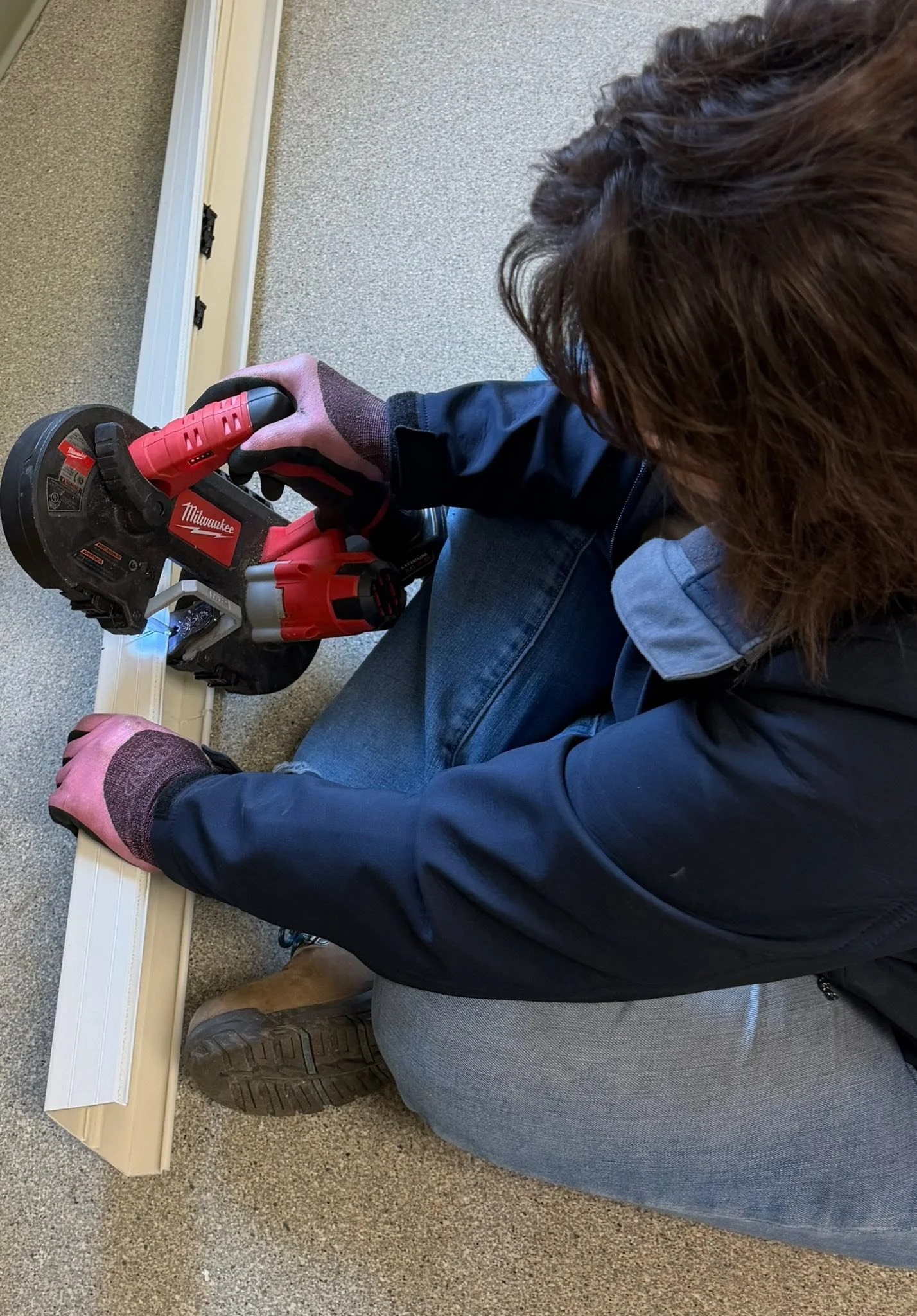 Person using a Milwaukee cordless circular saw to cut a piece of wood on the floor.