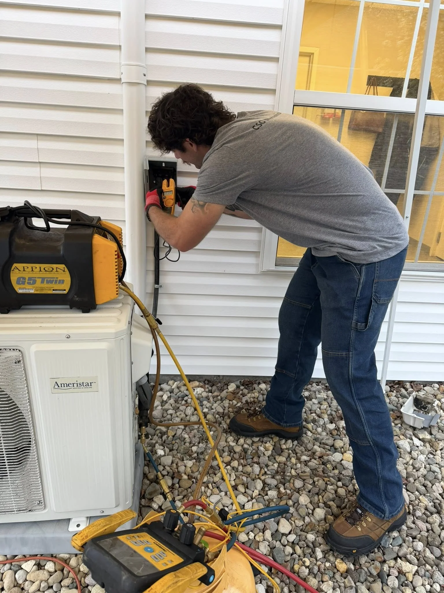 HVAC technician performing diagnostics on a residential outdoor AC unit, using gauges and testing equipment to identify potential issues and determine if air conditioner repair is needed.