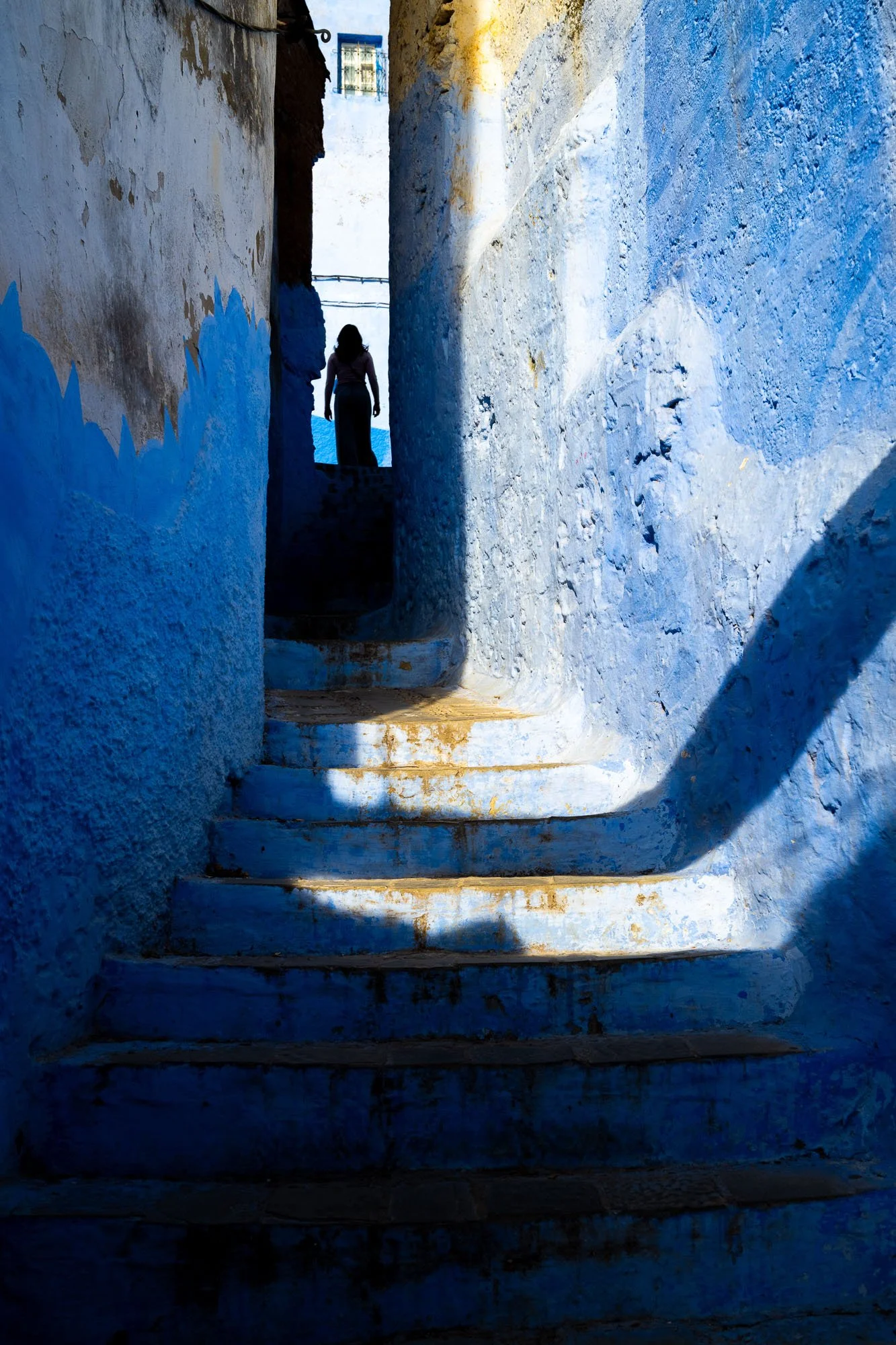 A silhouette of a figure in a sunlit blue alleyway in Chefchaouen, Morocco, demonstrating the Architecture of Absence and the Gestalt Law of Closure in photography