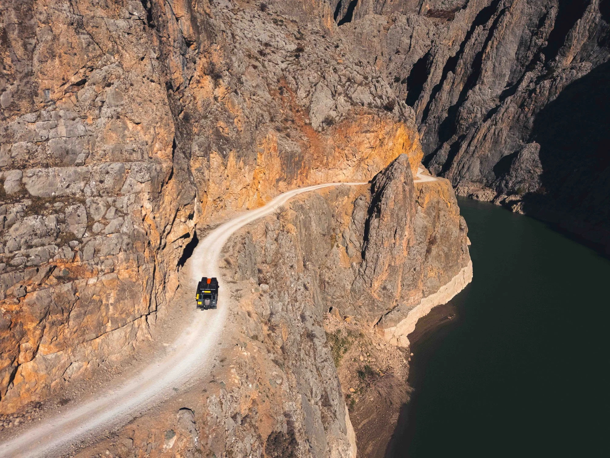 An aerial drone view of the hand-carved Tas Yolu stone road in Türkiye, with a vehicle on the precipice. This image demonstrates that true resilience is found when we refuse to accept a comfortable cage.