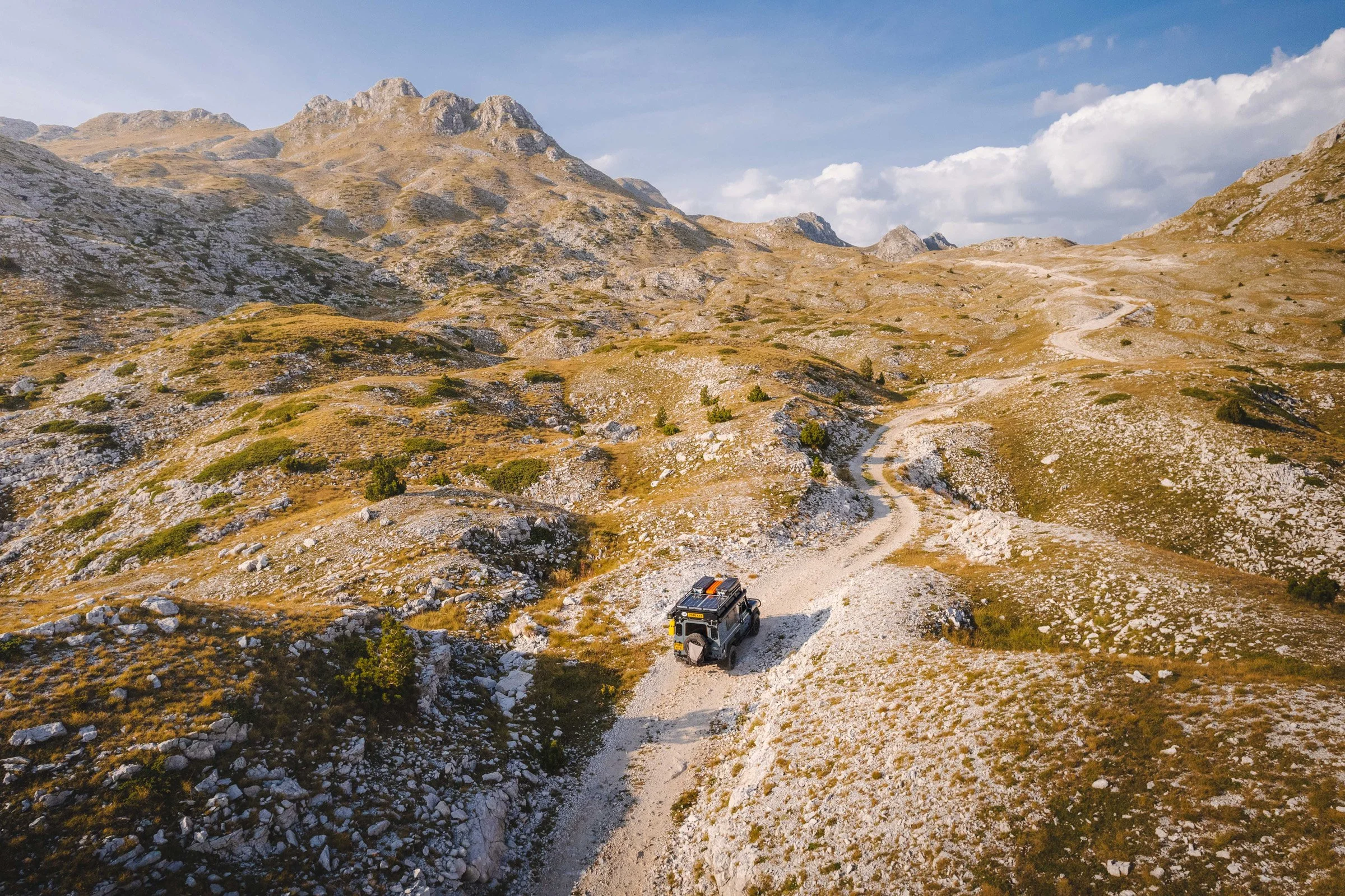 A Land Rover Defender navigating a rugged, winding mountain trail in Durmitor, Montenegro. This landscape illustrates the 'Internal Landscape' of the photographer, seeking solitude and resilience in the wild.