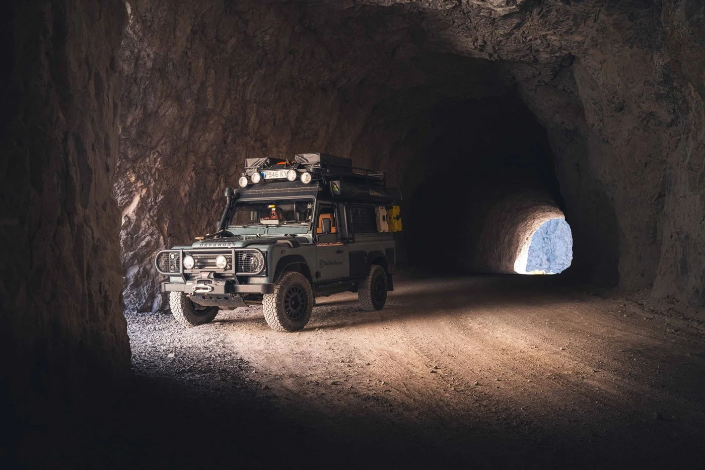 A Land Rover Defender enters one of the 38 unlit, hand-carved tunnels of the Tas Yolu (Stone Road) in Türkiye. The extreme chiaroscuro lighting creates intense visual tension and triggers bottom-up cognitive processing.