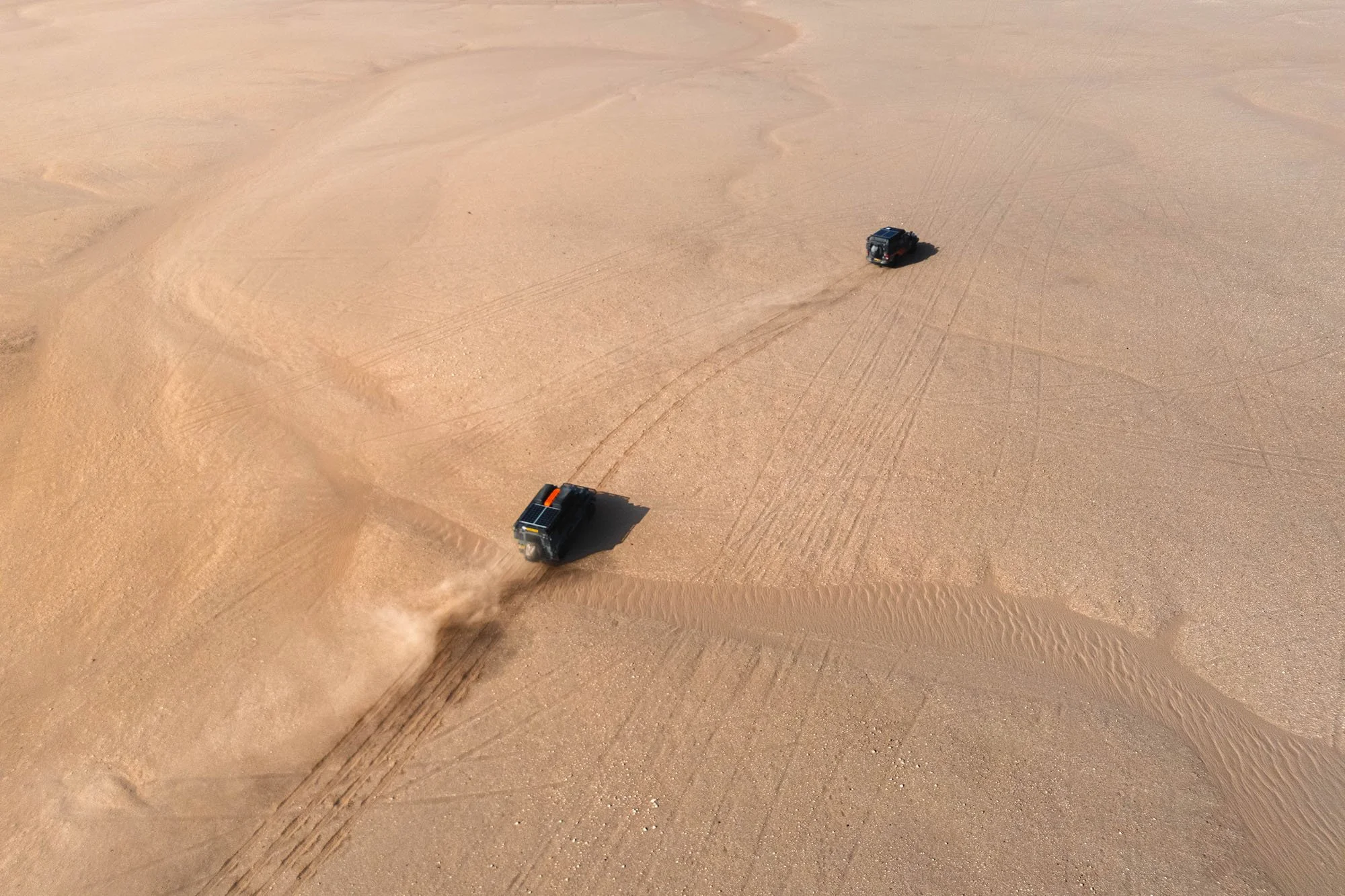 Deep sand ruts leading toward an expedition Land Rover Defender driving across the vast, arid desert expanse of Mauritania