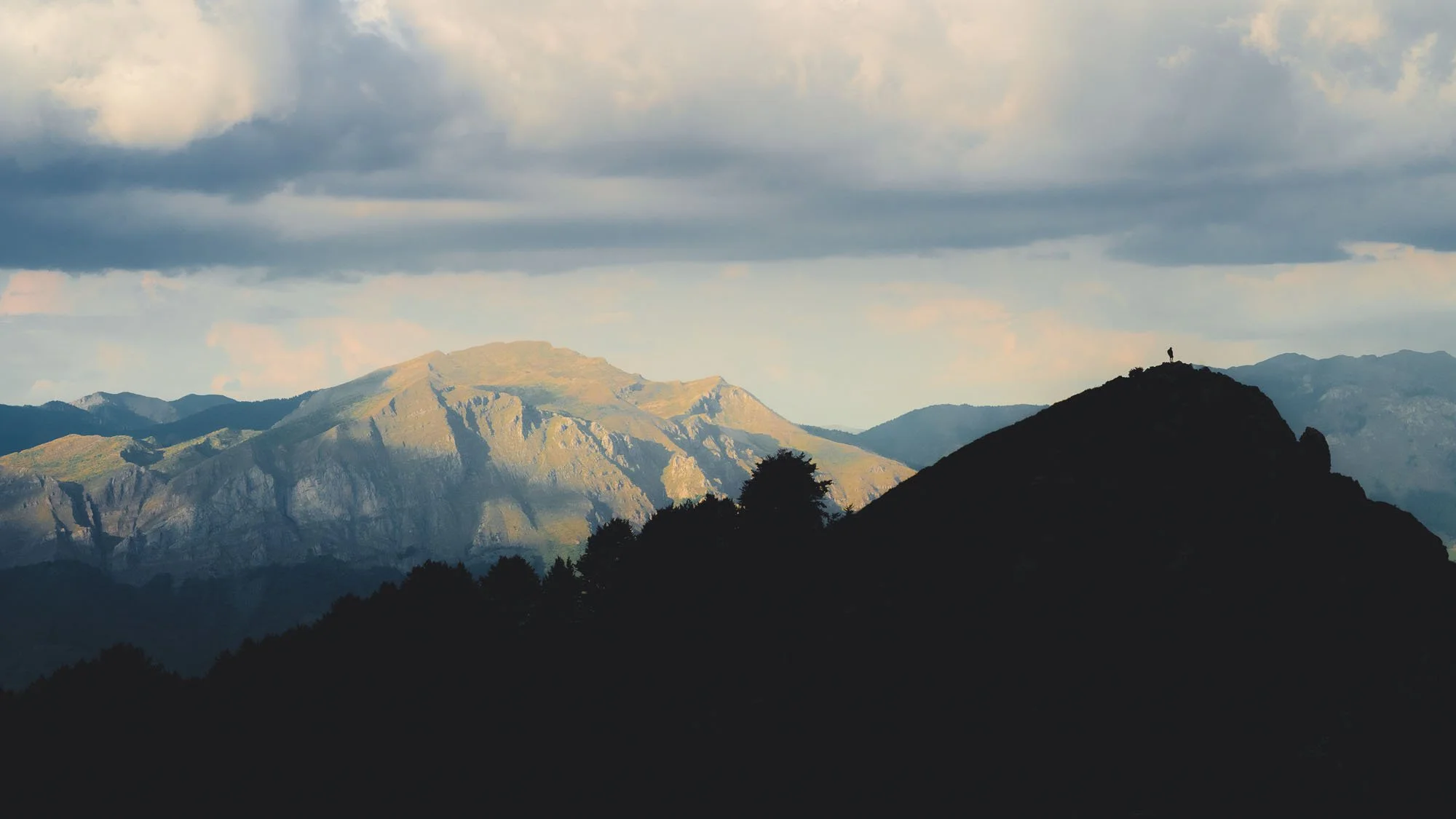 A total silhouette of a hiker on a mountain ridge in Vosunica, Montenegro, acting as a continuity trigger that forces the brain to mentally draw the rest of the landscape