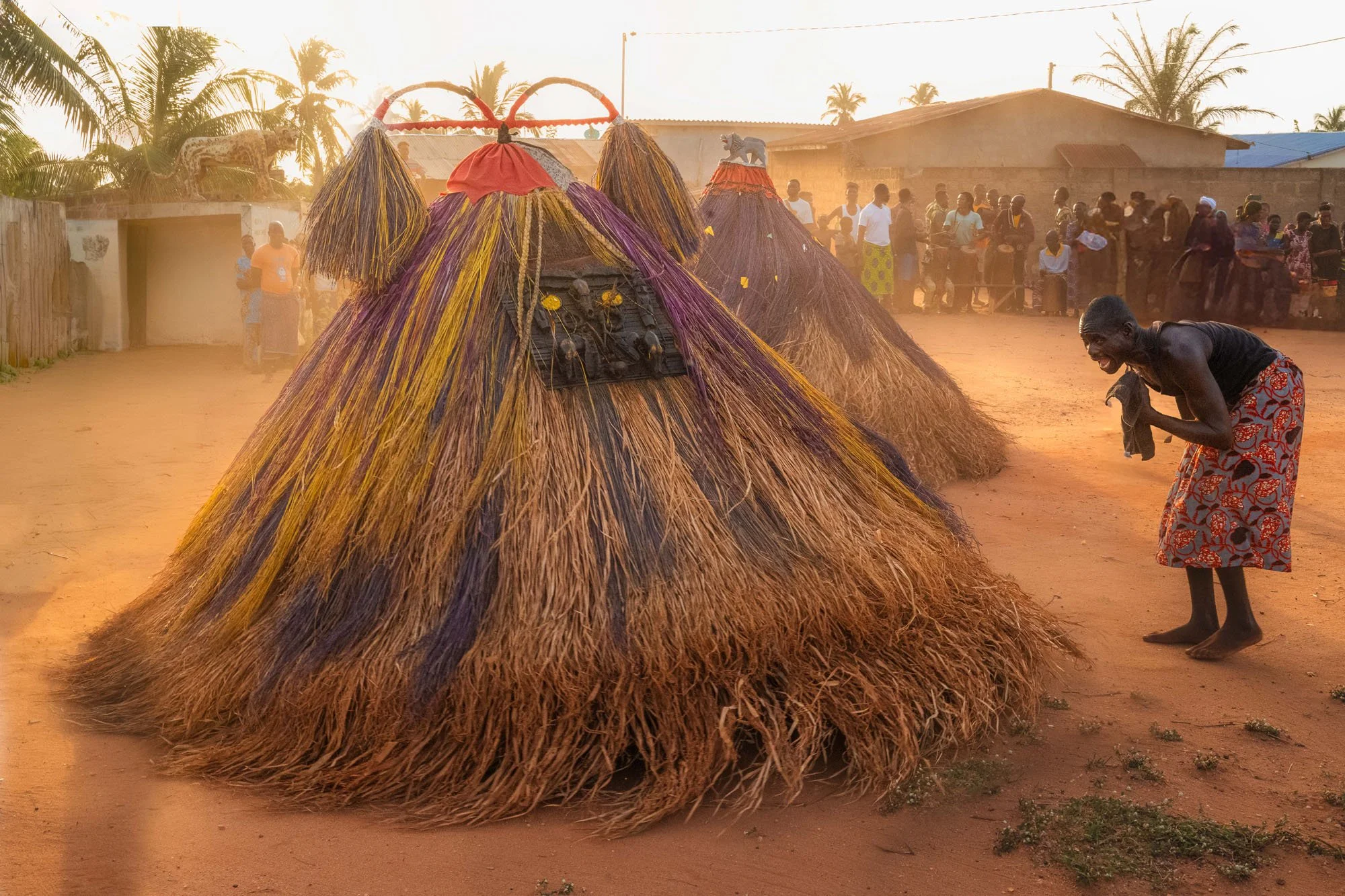 A bare-chested village minder shouting and gesturing in trance toward a spinning straw Zangbeto in a rural clearing in Benin