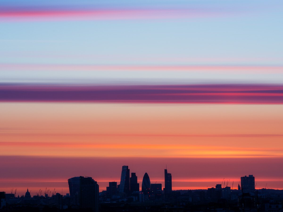 The London financial district skyline in dark silhouette against an abstract, painterly sunset sky with horizontal streaks of pink, violet, and orange