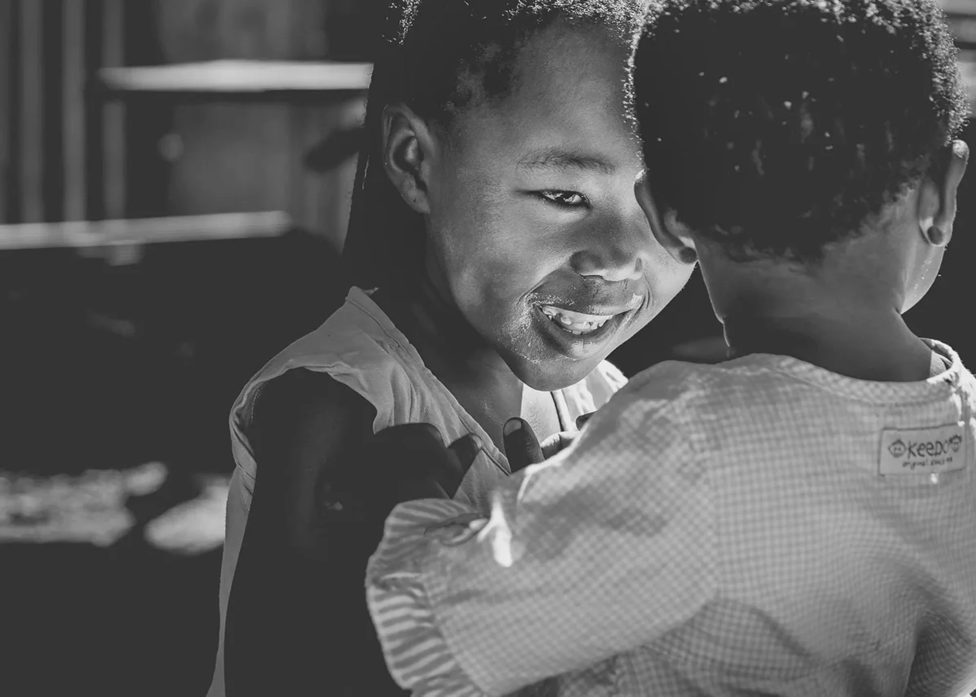 A black and white candid portrait of two children smiling in Langa Township, South Africa. This image utilizes mirror neurons to create biological synchronization and an immediate emotional connection with the viewer.