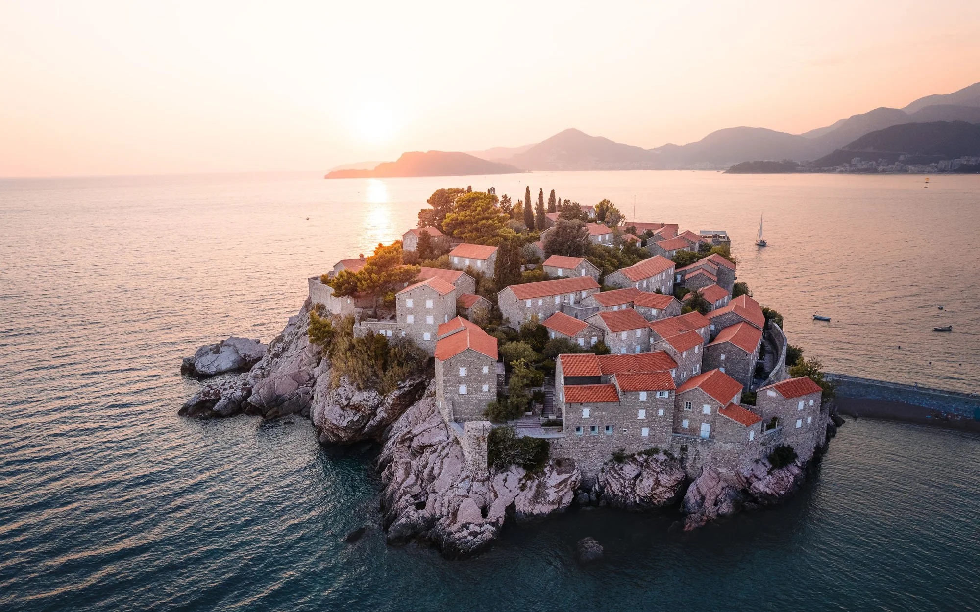 An aerial drone view of Sveti Stefan island in Montenegro at sunset. The geometric symmetry and warm light appeal to the brain's preference for visual order and psychological safety