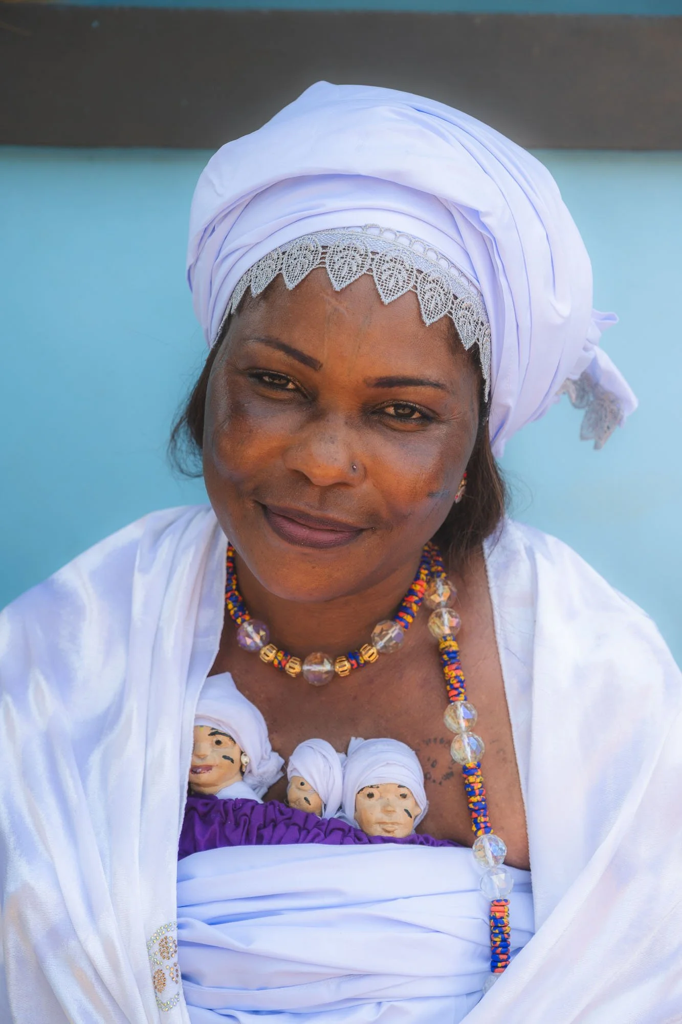 Close-up portrait of a smiling female Mami Wata acolyte wearing traditional white clothing and beaded necklaces.