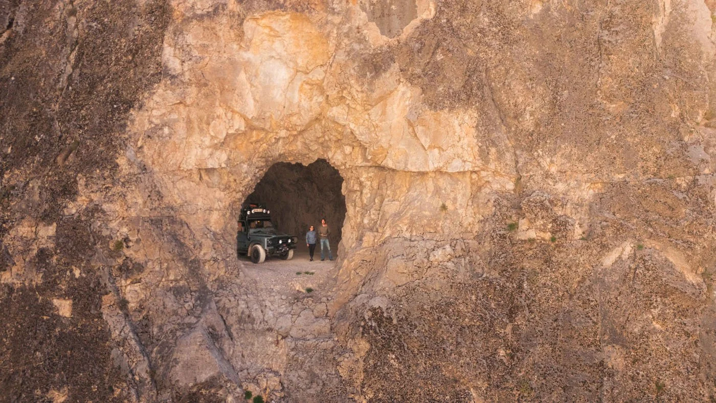 An aerial view of the Land Rover Defender parked inside a hand-carved 'window' of the Tas Yolu stone road, looking out into the Karanlik Kanyon abyss. This extreme use of human scale highlights the ingenuity and grit of the local community.