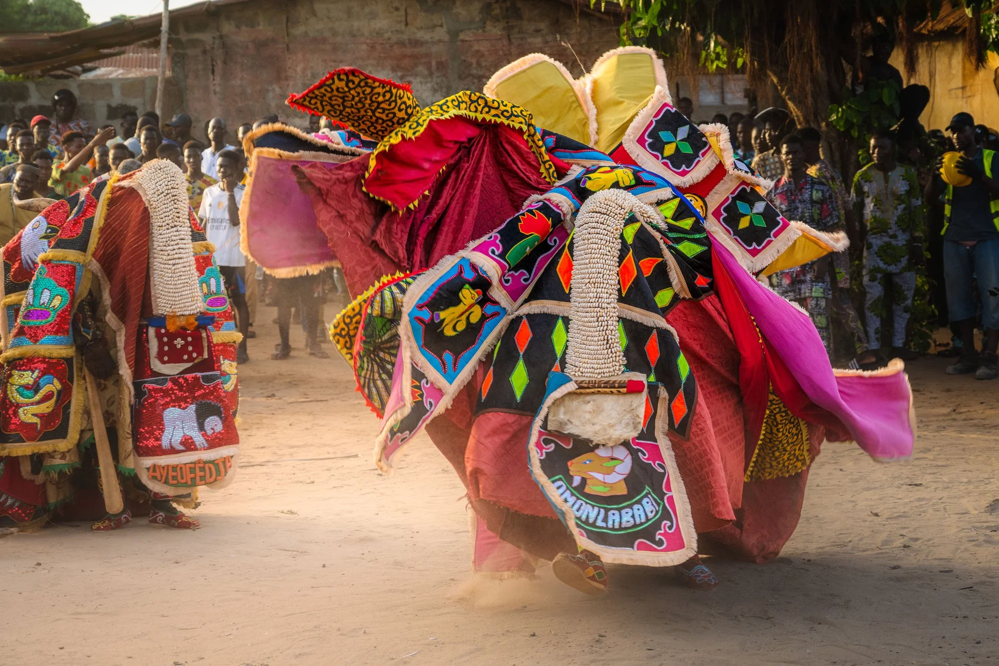 An Egungun spirit in a vibrant, multi-colored costume performs at a Voodoo ceremony in Benin. The explosive movement and swirling dust capture extreme kinetic energy, triggering rapid bottom-up processing in the viewer's brain.