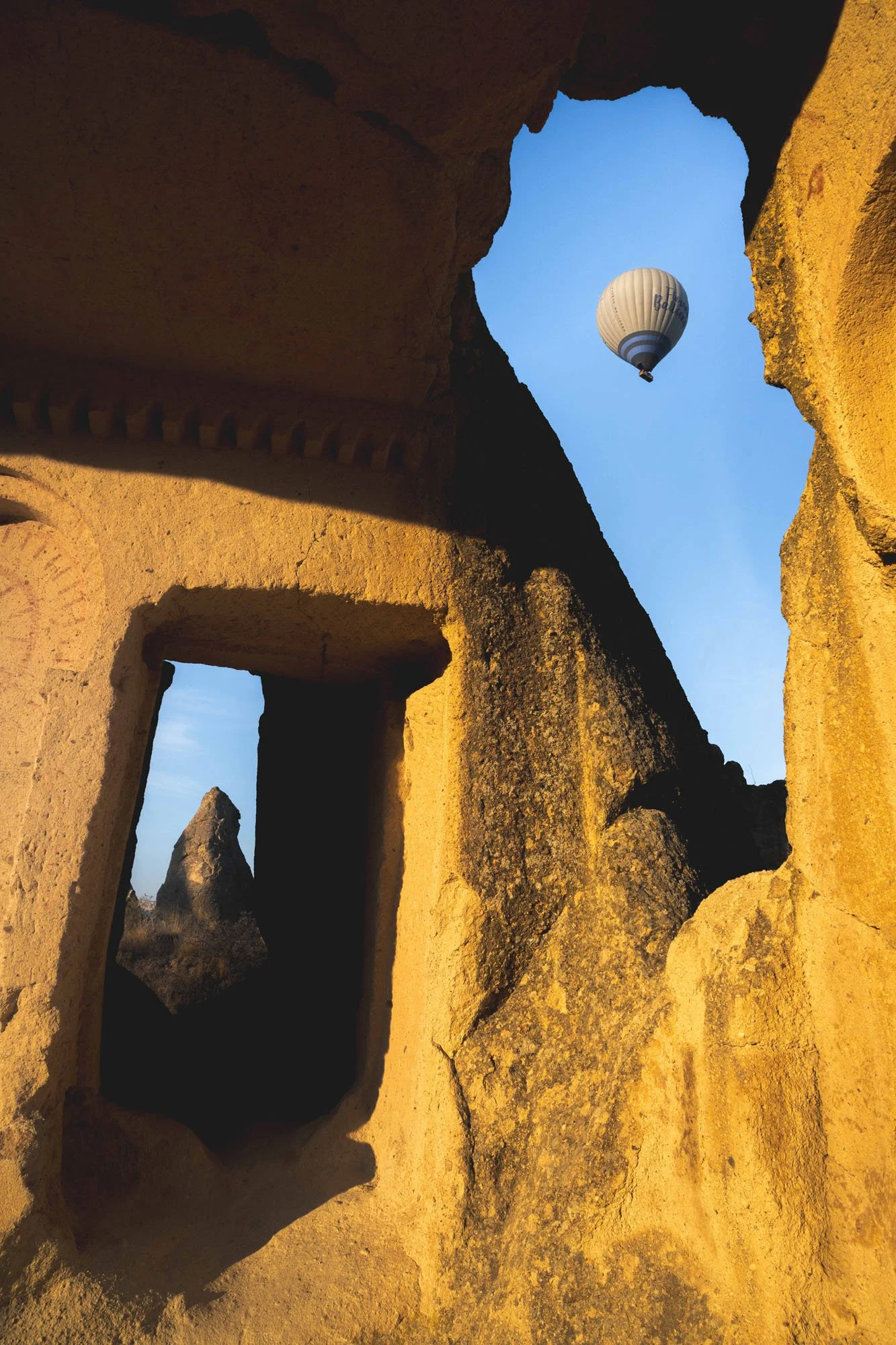 A single hot air balloon framed perfectly through a sharp, weathered rock archway in Cappadocia, showing the relational friction between geometric shapes and natural stone