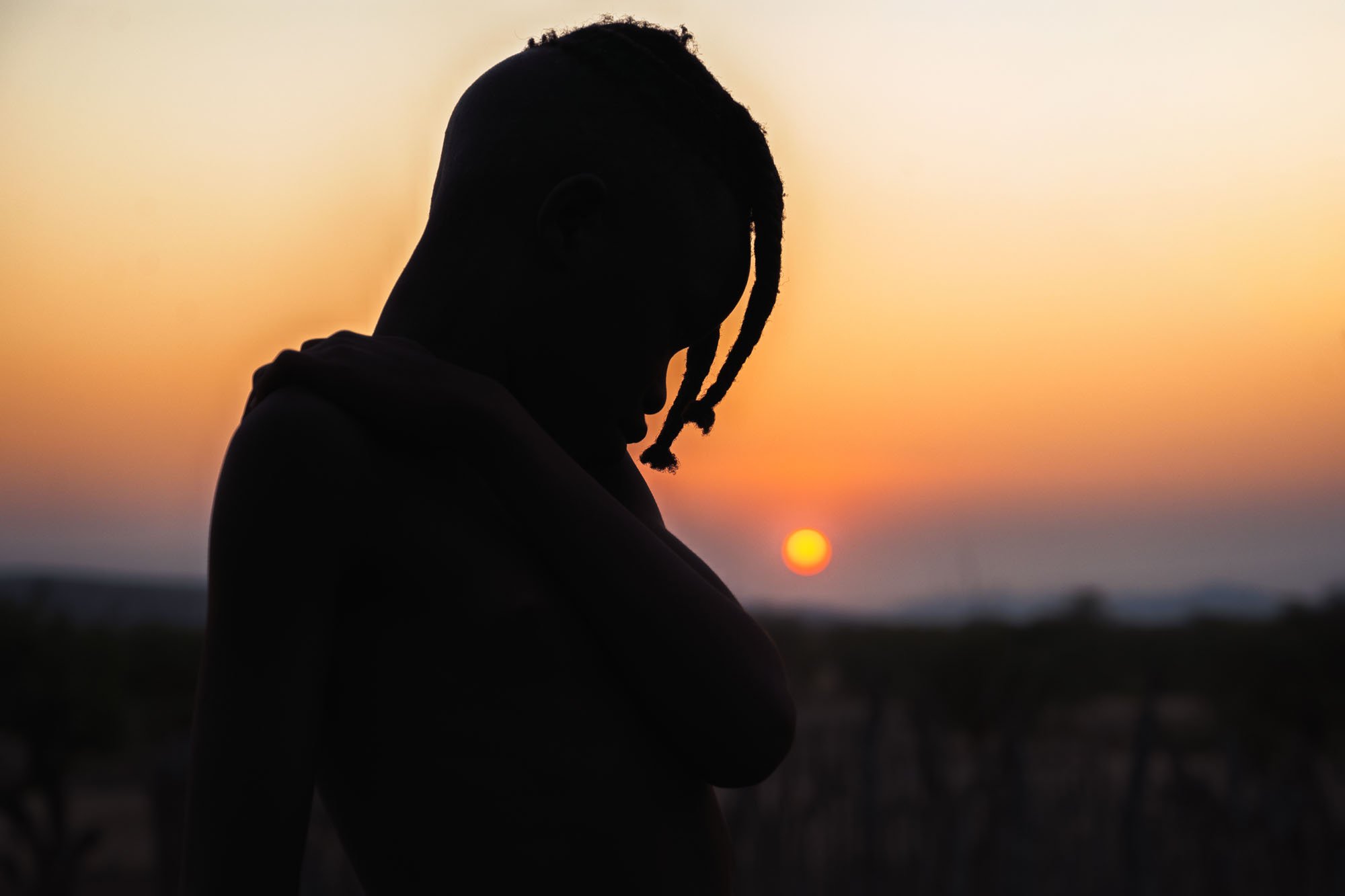 A silhouette of a young Himba person against a sunset in Namibia. This is a practical example of the Law of Prägnanz, where the brain organizes a complex human subject into its simplest, most impactful form.