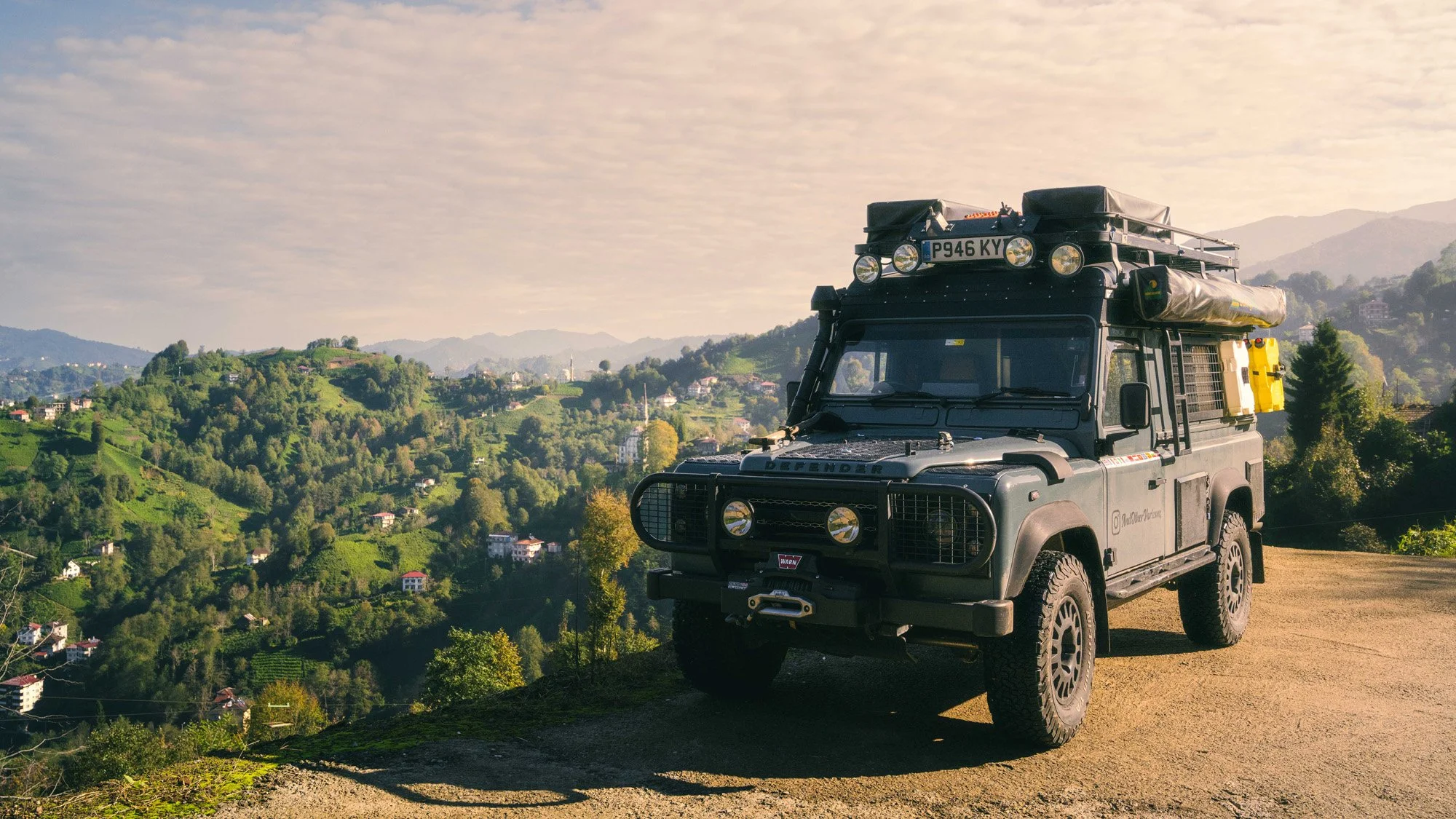 A Land Rover Defender parked on a high mountain overlook in Haremtepe, Eastern Türkiye, with rolling green hills in the background. The composition uses the vehicle as a visual anchor to provide narrative context to the vast landscape.