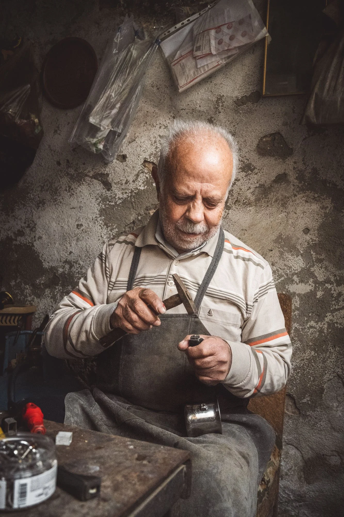 Portrait of an elderly coppersmith with a white mustache working metal with a hammer in his workshop in Mardin, Turkiye.
