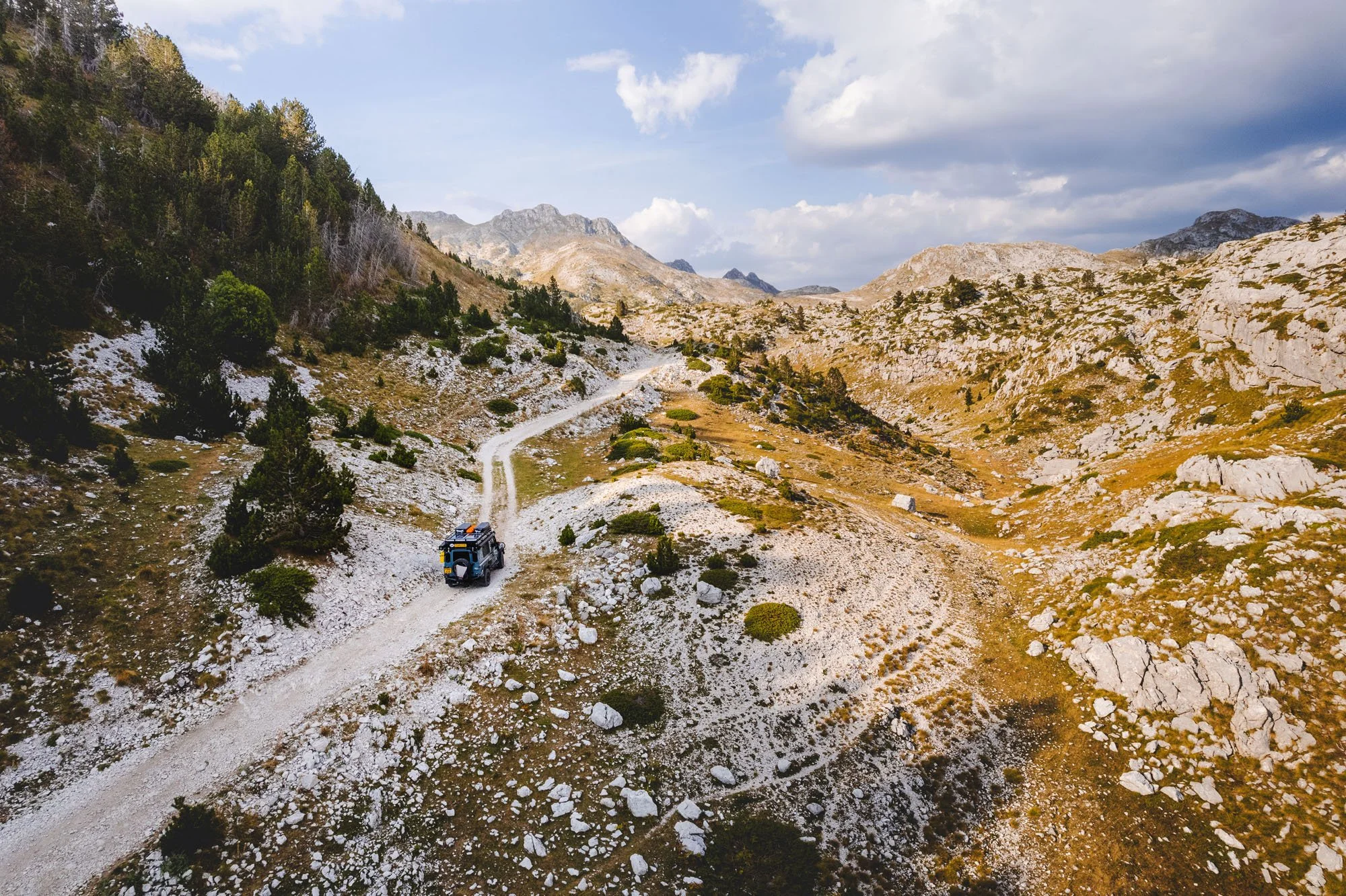 An expedition-equipped Land Rover Defender driving along a remote, rocky mountain ridge track in Durmitor National Park, Montenegro.