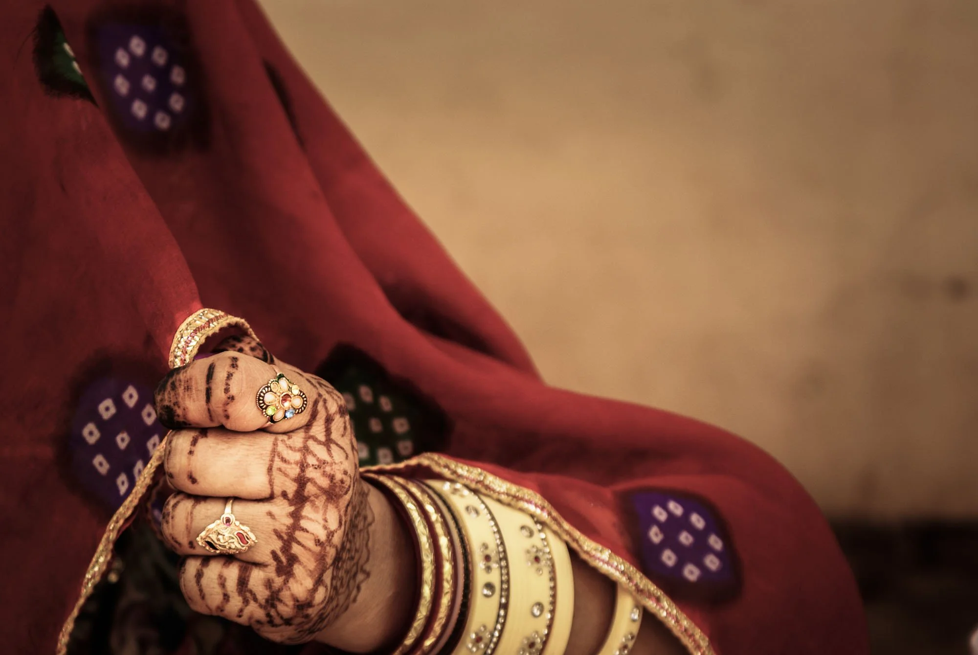 A close-up of a hand adorned with Mehndi and bangles gripping red fabric in India. This image utilizes 'Isolated Tension' to leave unanswered questions, forcing the viewer's brain to actively engage and close the narrative loop.