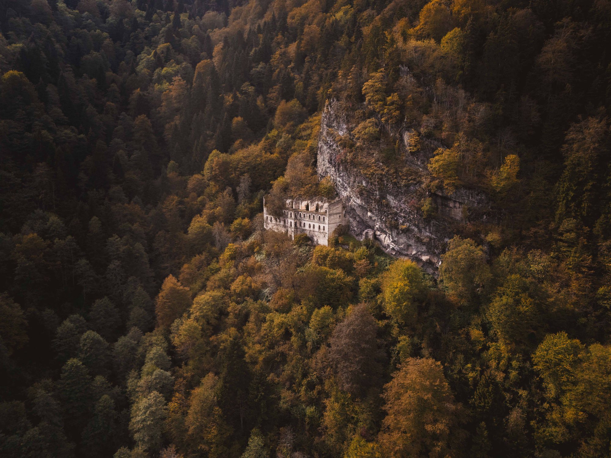 An aerial view of the ancient Vazelon Monastery built into a cliffside surrounded by autumn forests in Türkiye, demonstrating how the brain forces a story onto a scene.