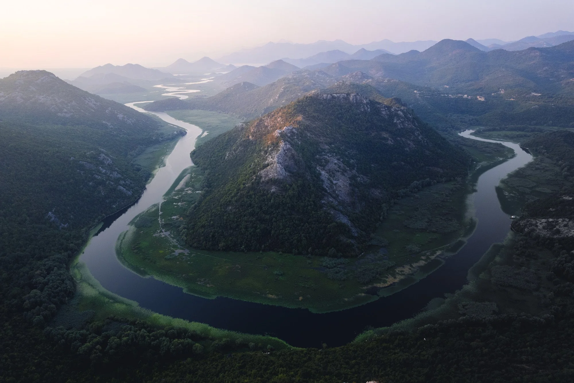 The famous Pavlova Strana horseshoe bend of the Crnojević River near Lake Skadar, Montenegro. The winding river acts as a powerful natural leading line, guiding the viewer's eye through the misty mountain landscape.