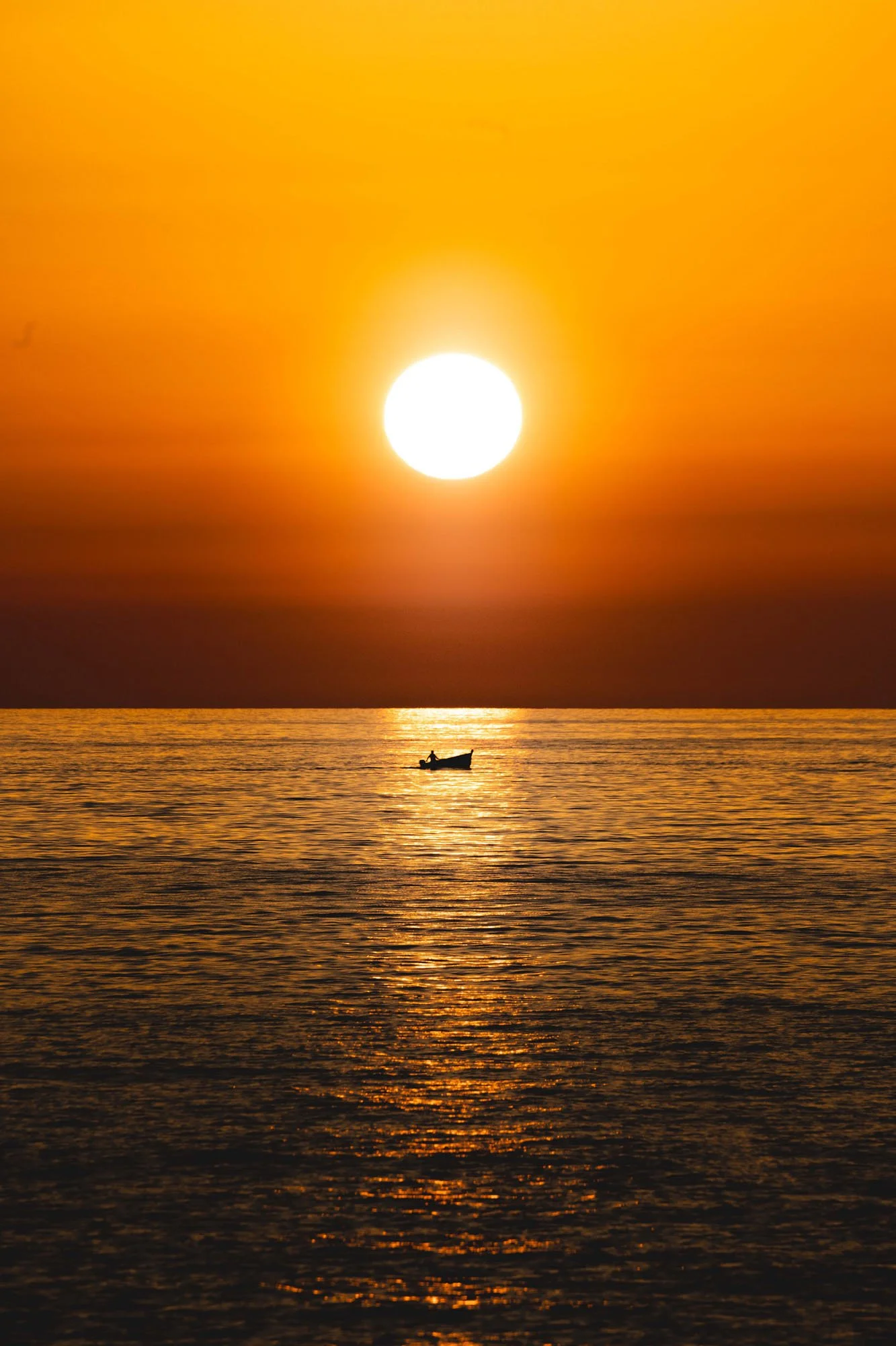 Silhouette of a small boat on the ocean during a vibrant orange sunset off the coast of Italy.