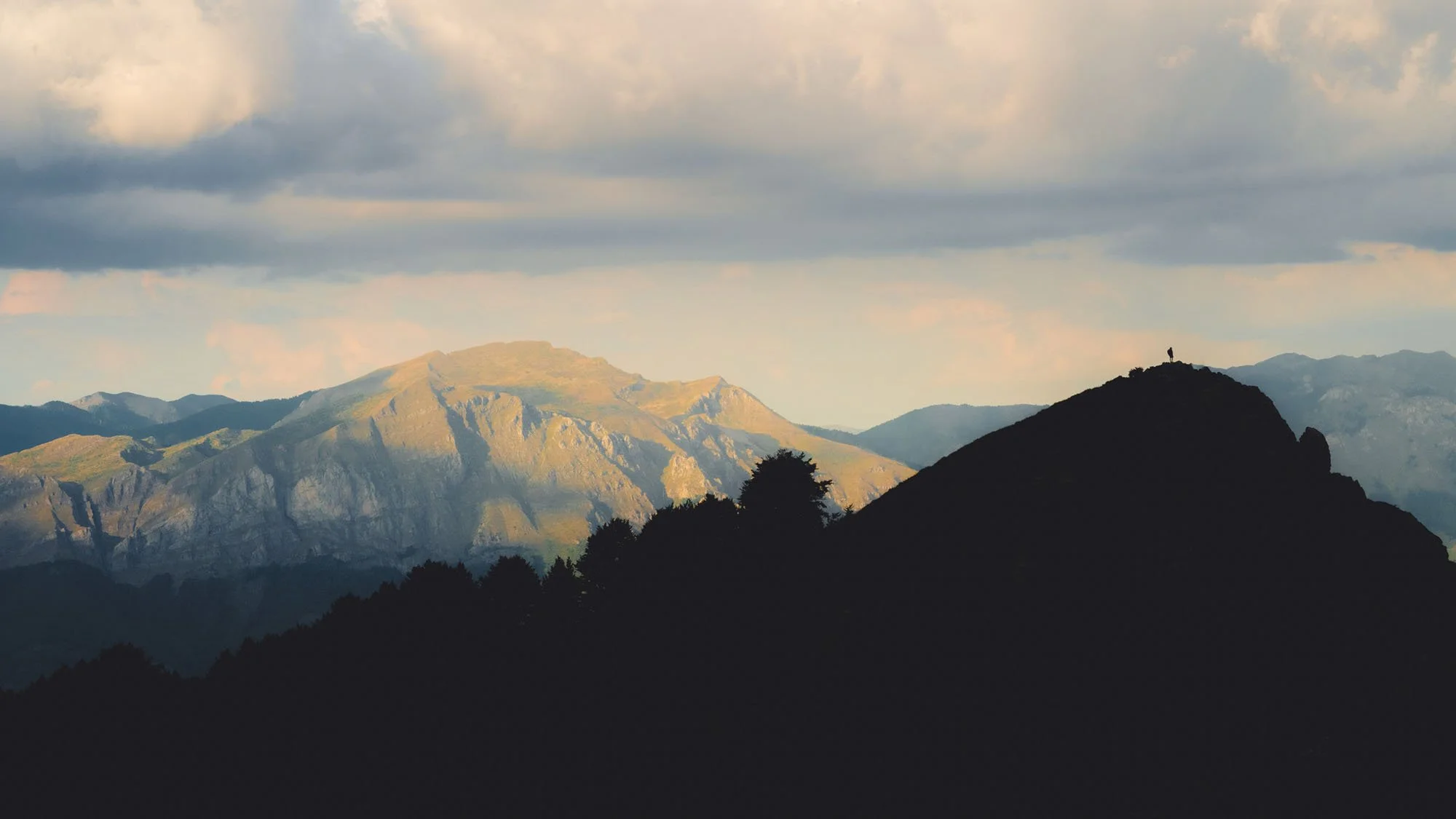 A tiny human silhouette stands on a sharp mountain ridge in Prokletije National Park, Montenegro. The high figure-to-ground contrast and vast empty space illustrate the psychological concept of the 'Impossible Vastness' in photography.