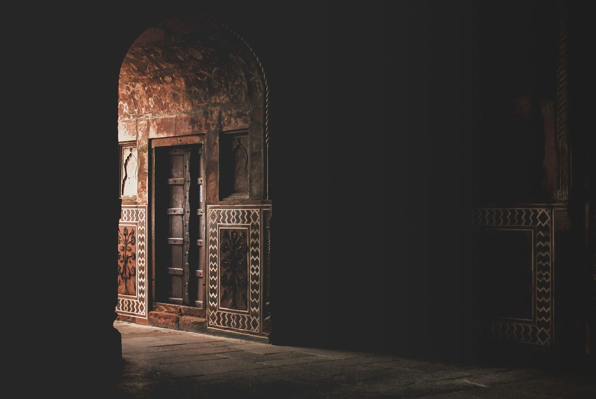 An intricately carved stone archway in India leading into total darkness. This visual represents 'The Void'—the psychological state of having too little information to anchor viewer engagement