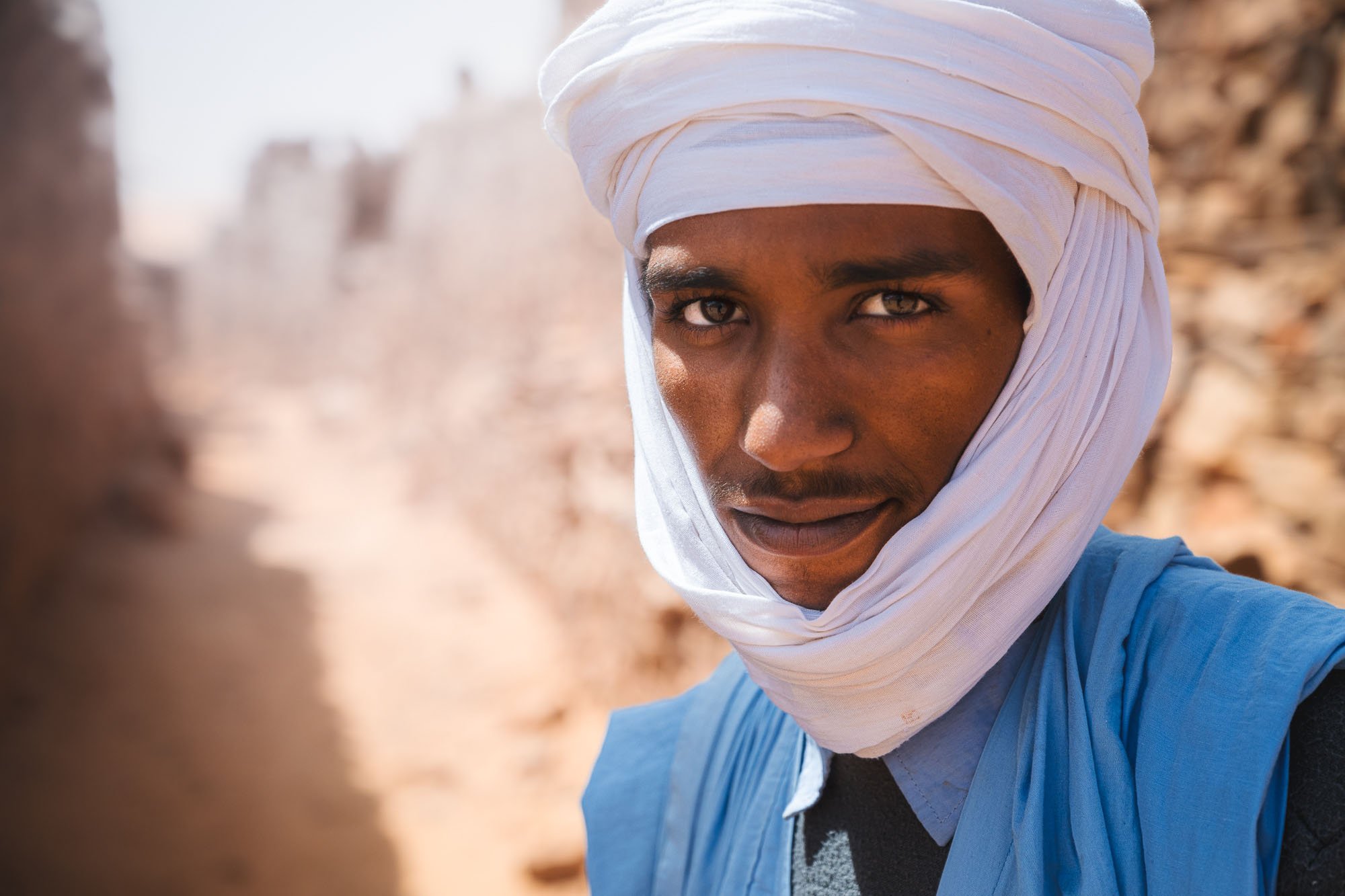 A close-up portrait of a Bedouin man in a blue turban and white headscarf in the Sahara Desert, illustrating the psychological gaze and cognitive empathy in portrait photography.