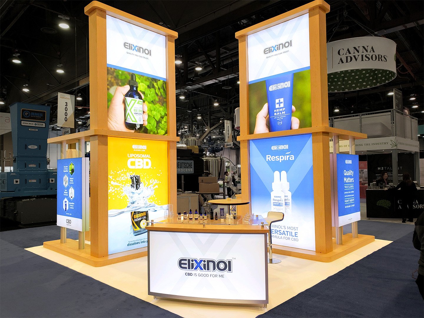 Trade show booth displaying CBD products by Elixinol with bright posters of CBD oil bottles and information about hemp and CBD benefits.