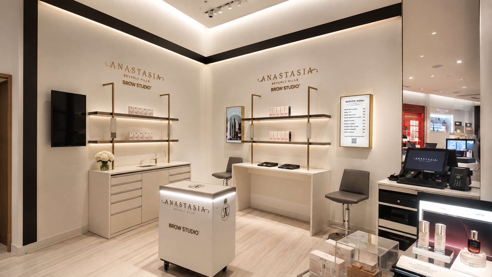 Interior of an Anastasia Beverly Hills Brow Studio with white walls, gold accents, a service menu, a computer, and shelves with beauty products.