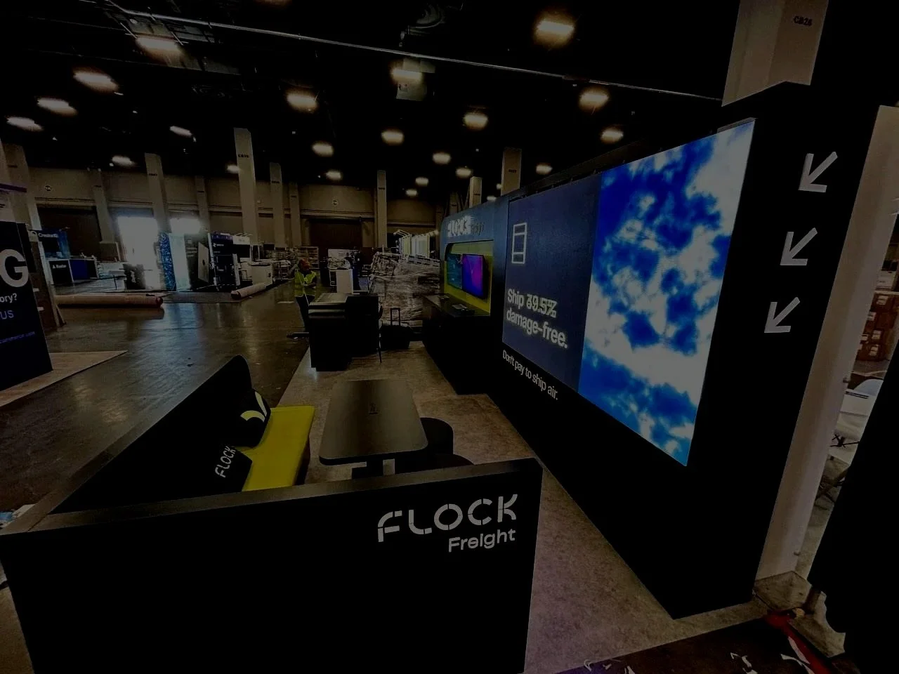 Empty airport baggage claim area with a large digital screen displaying clouds and the word 'FLOCK' on the side of the conveyor belt.