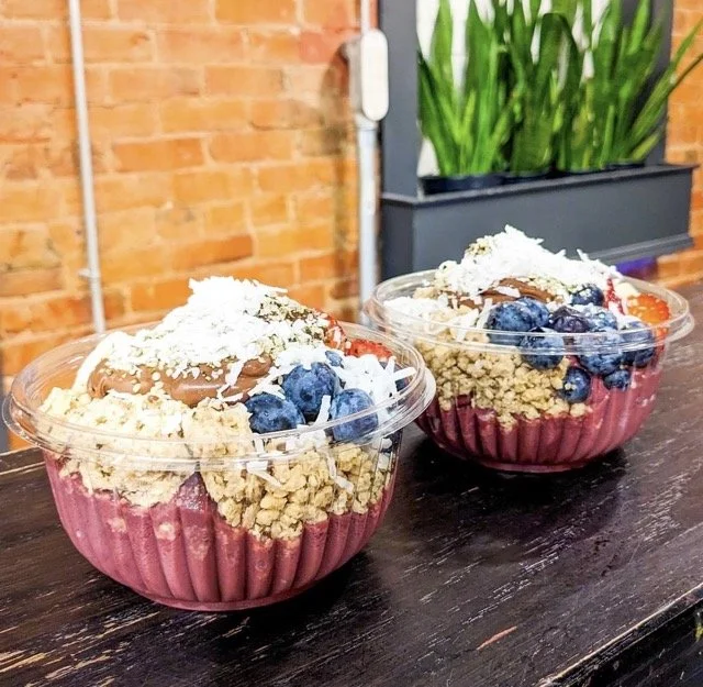 Two bowls with fresh ingredients, including blueberries, sitting on a wood table.