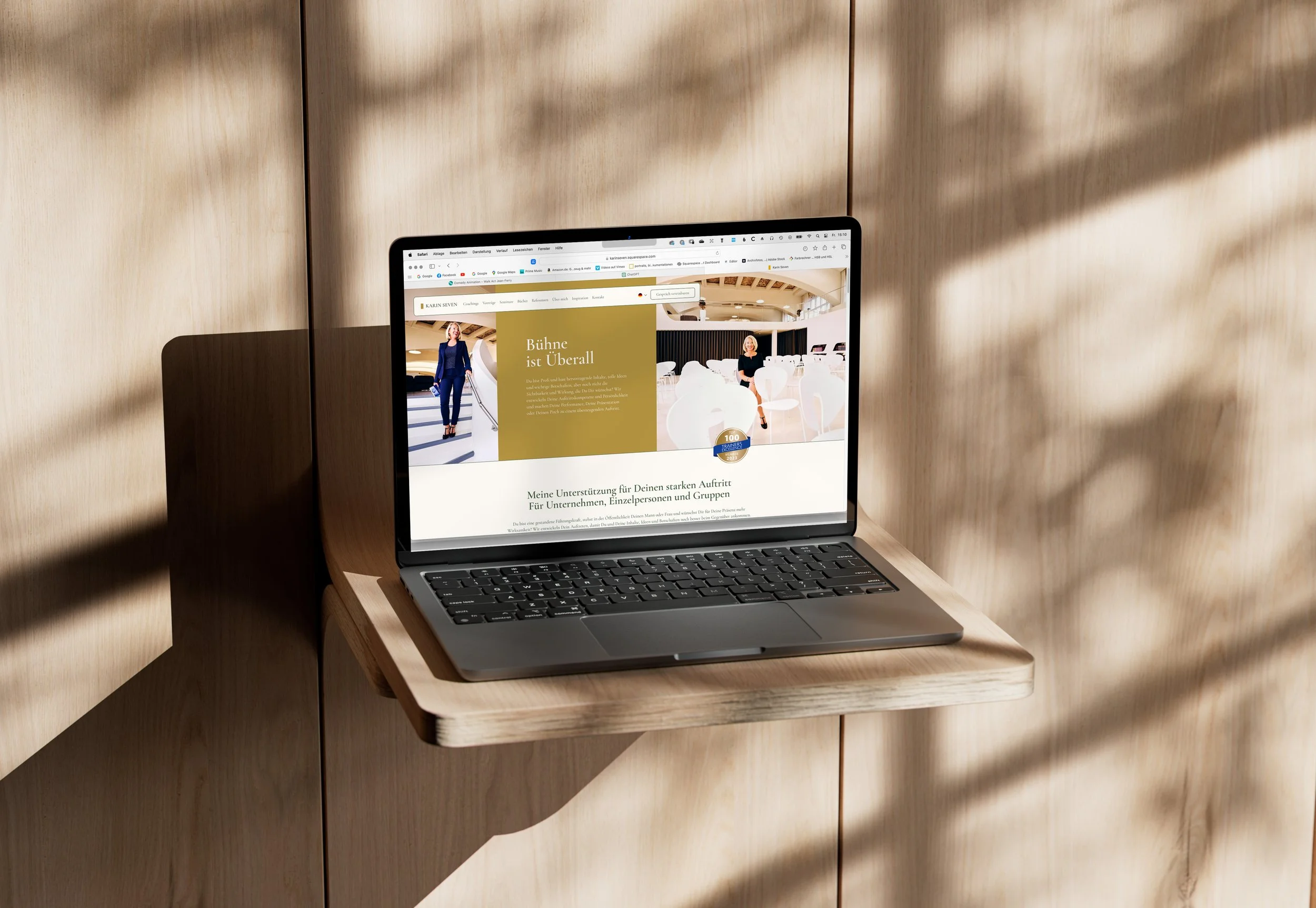 Ein Laptop auf einem kleinen Holzregal mit Schatten von einem Fenster und einem Baum im Hintergrund.