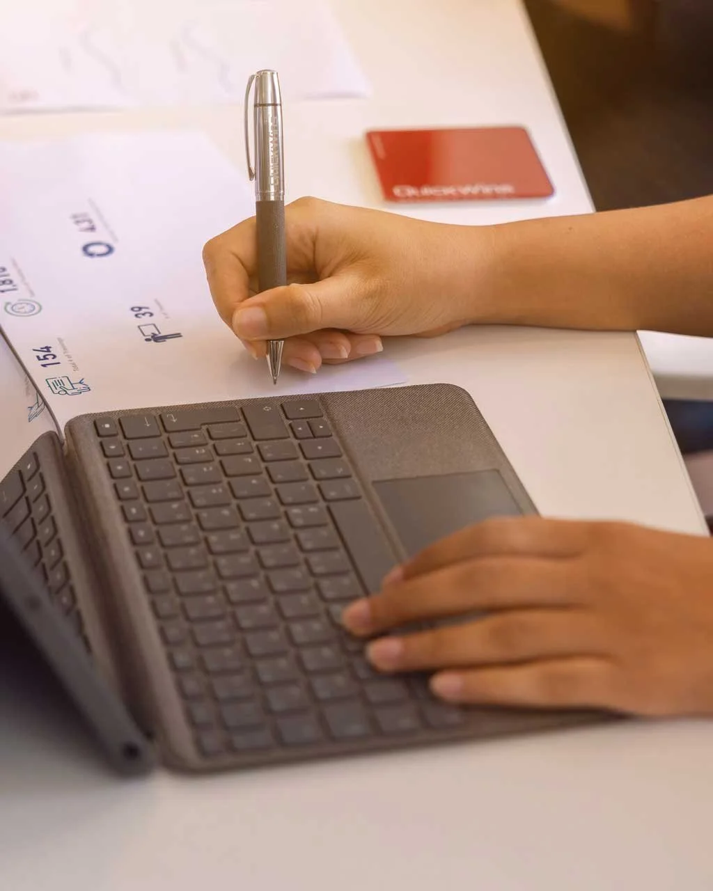 A hand writing notes on printed charts beside a tablet keyboard.