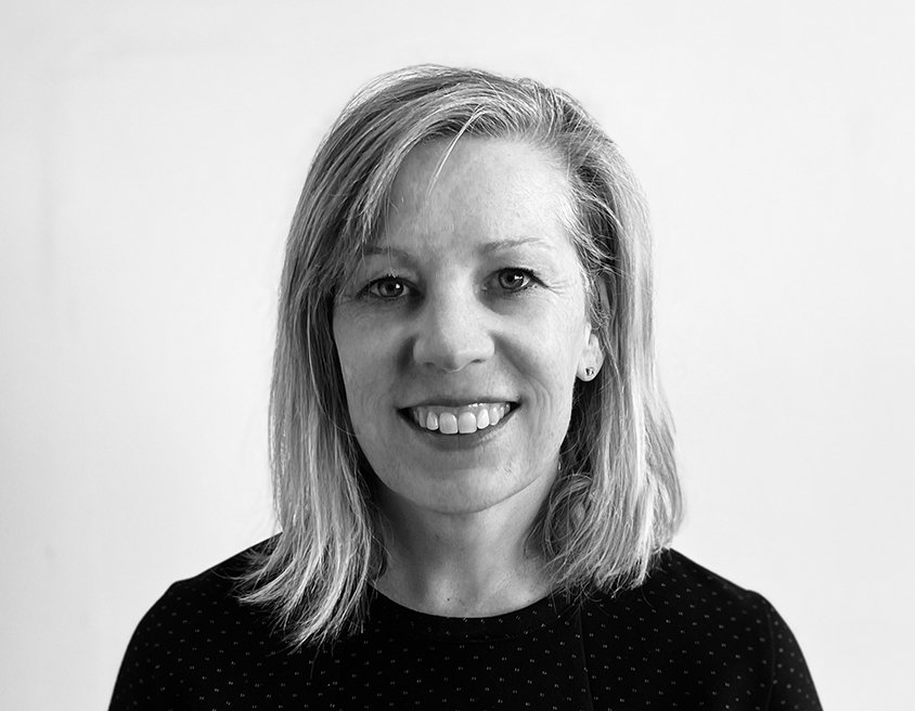 Black and white portrait of a smiling woman with shoulder-length wavy hair, wearing a black shirt.