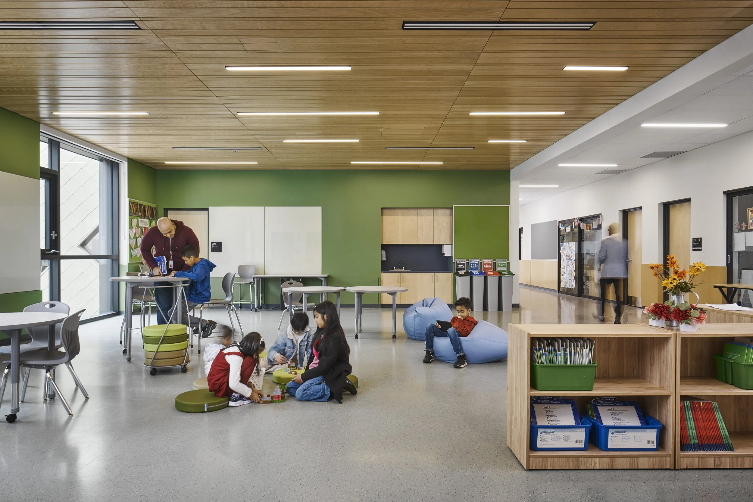 Rendering of a modern, colorful school building with children playing outside in a courtyard with a tree, benches, and urban furniture.