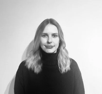 Black and white photo of a young woman with shoulder-length wavy hair, wearing a turtleneck sweater, smiling slightly.