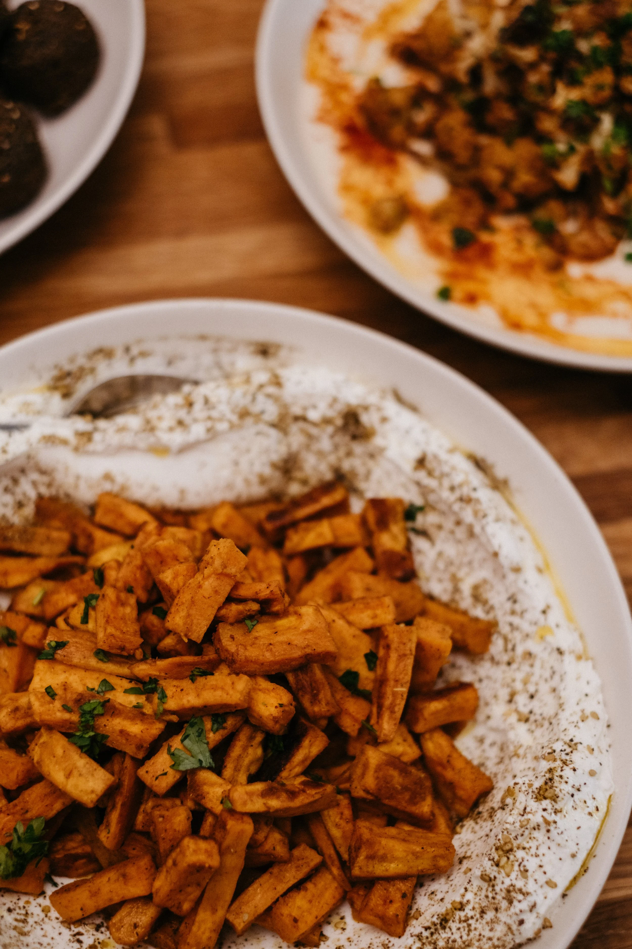 Close-up of a plate of spiced sweet potato and labneh with parts of other plates of food visible in the background.