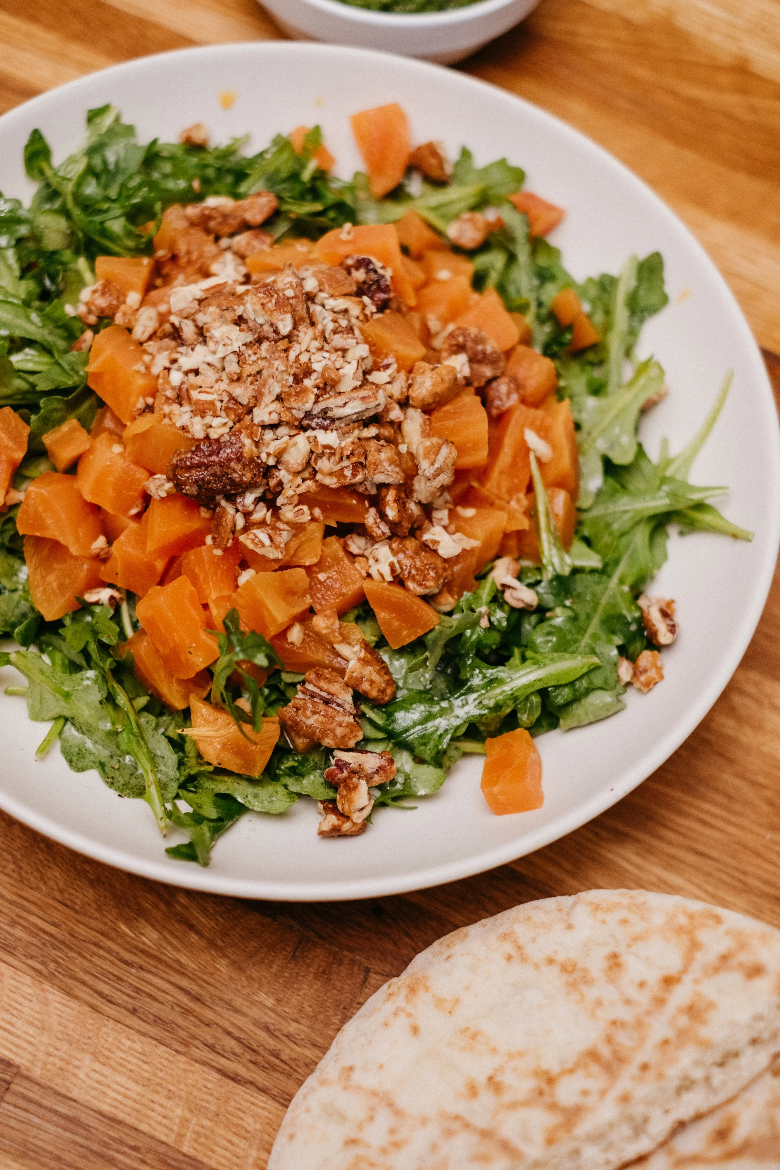 Beat salad with arugula, crushed pecans, and a side of pita bread on a wooden table.