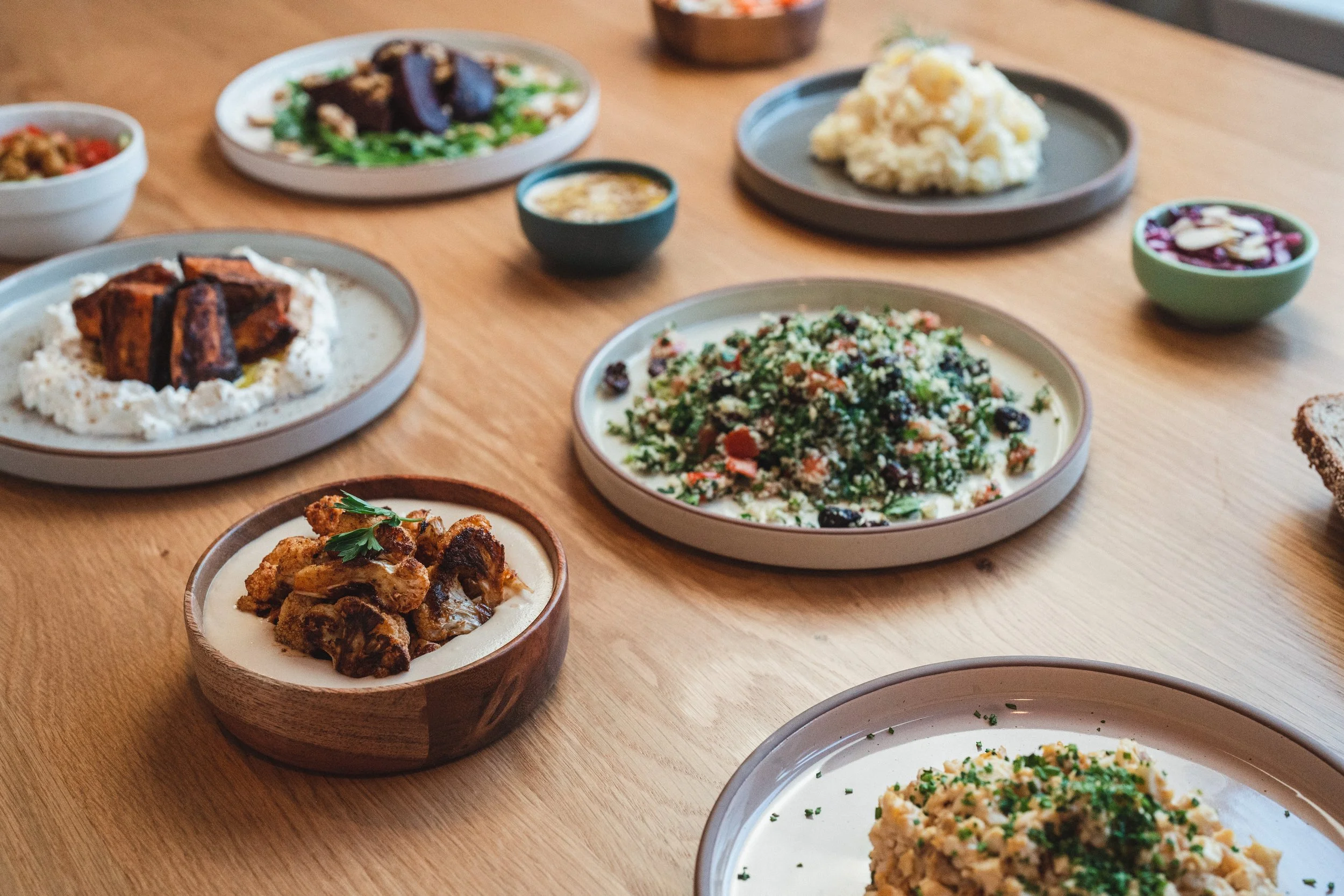 A spread of Middle Eastern dishes on a wooden table, including salads, dips, and roasted vegetables.