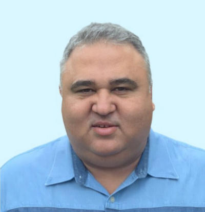 Joe Souza, part of The Well Coffee House's board of directors, wears a light blue button-up shirt against a light blue background.